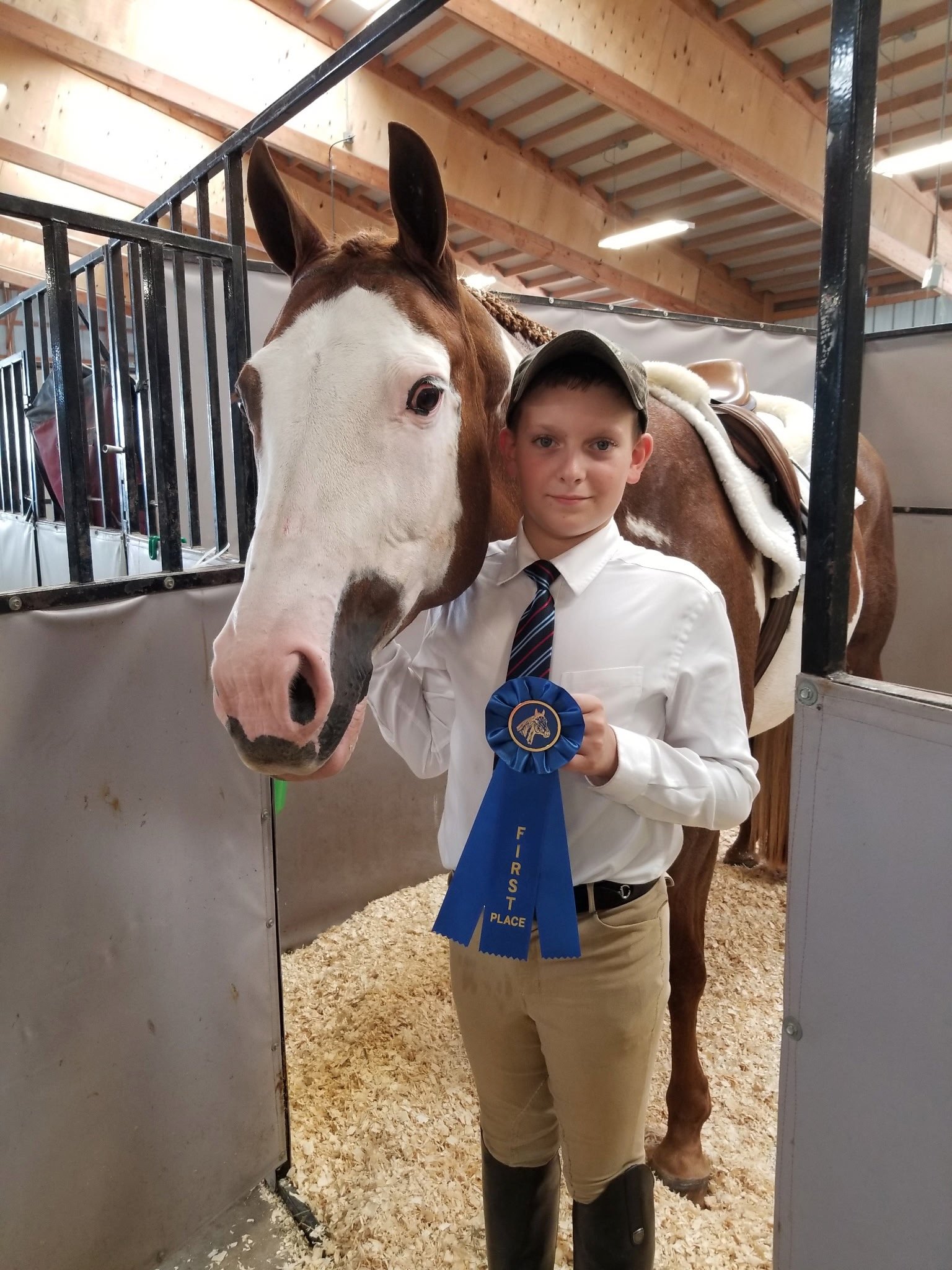 Young rider holding a first-place ribbon beside a horse at Shallow Creek Stables