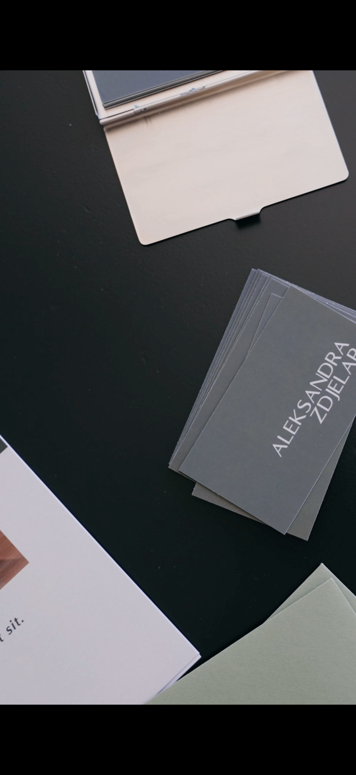 Business cards on a black table, one with the name 'Aleksandra Zdiar' and some papers and notebooks around.