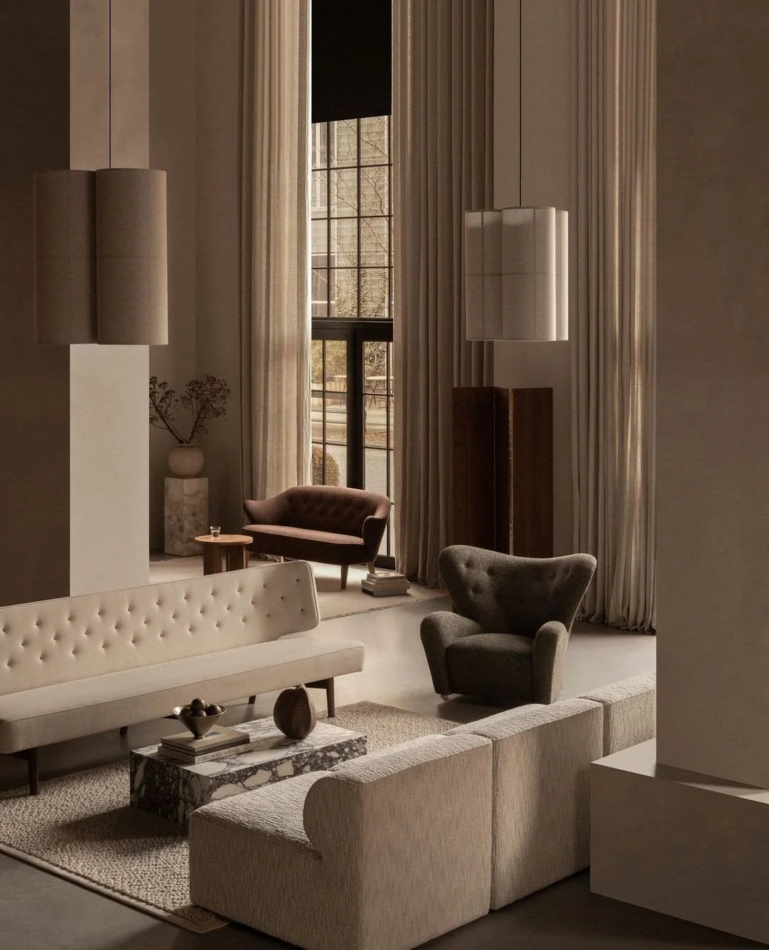 Elegant living room with high ceilings, large windows, beige curtains, modern furniture including a cream sofa, gray armchair, and a small side table, decorated with vases and books.