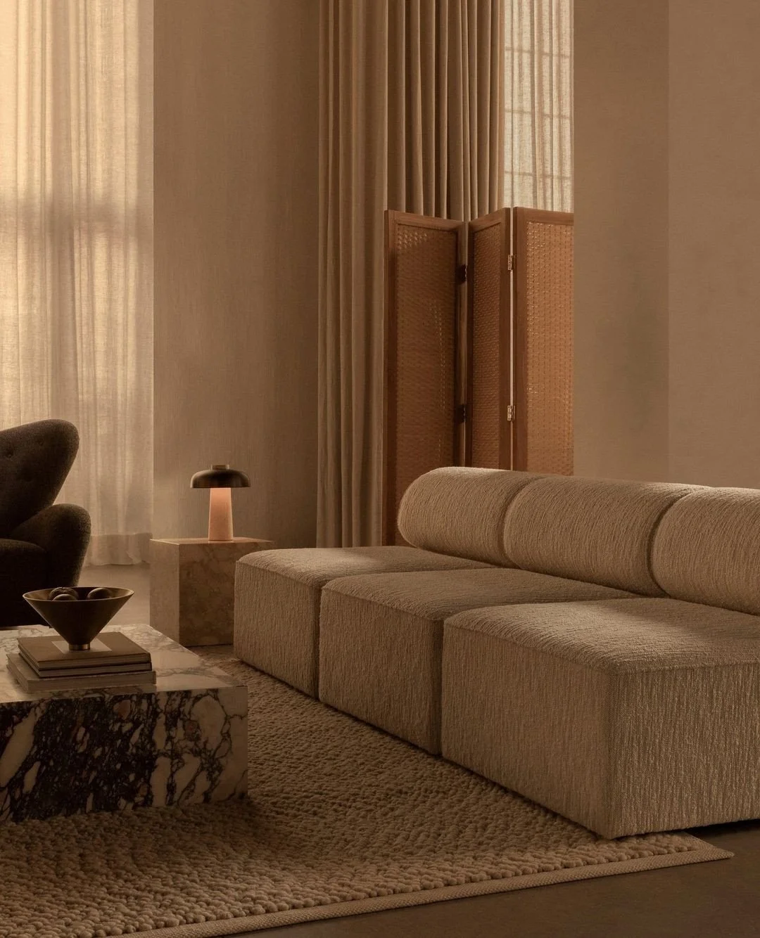 Living room with beige sofa, marble coffee table, wooden room divider, small table lamp, and layered curtains.