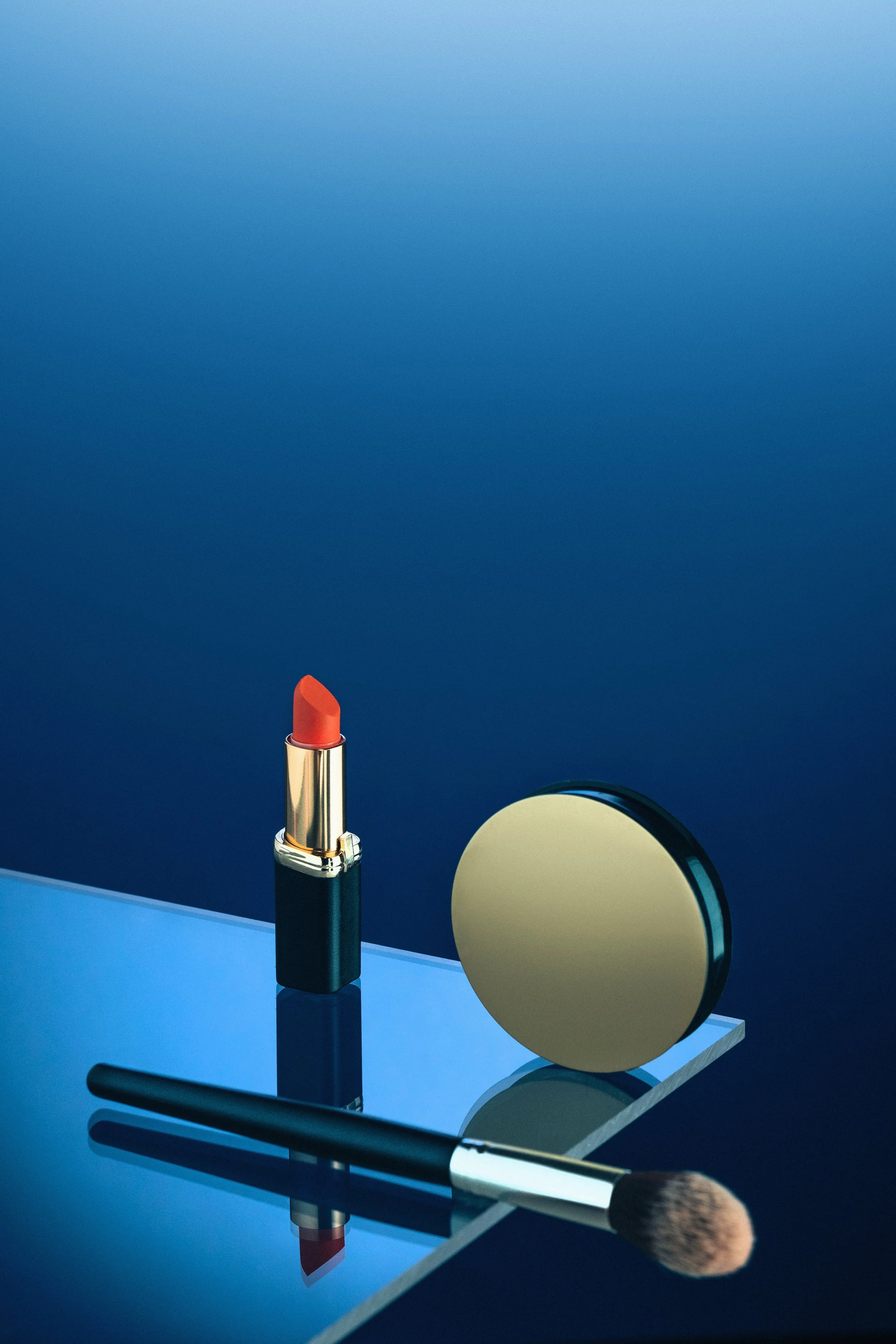 A collection of makeup items including a lipstick, makeup brush, compact mirror, and a butterfly-shaped mirror on a reflective surface against a blue background.