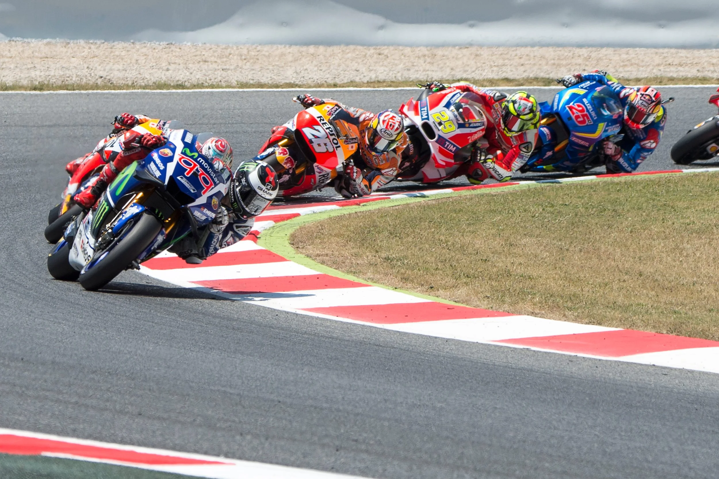 Motorcycle racers leaning into a turn on a racetrack, with colorful racing suits and helmets, riding sport bikes.