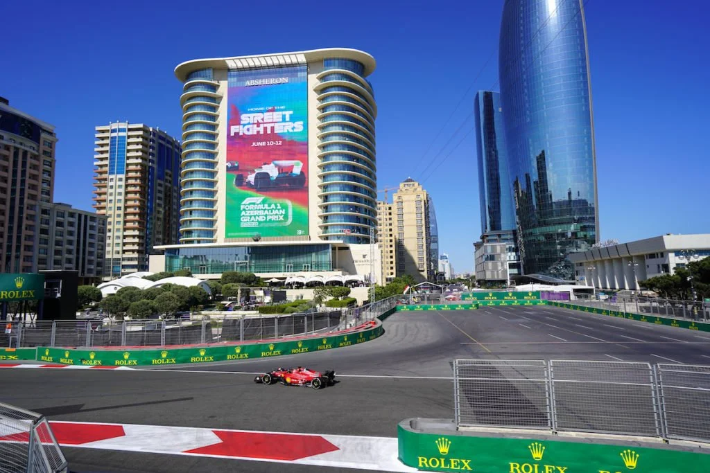 A Formula 1 race car on a street circuit in front of tall modern buildings and a large billboard in a city setting.