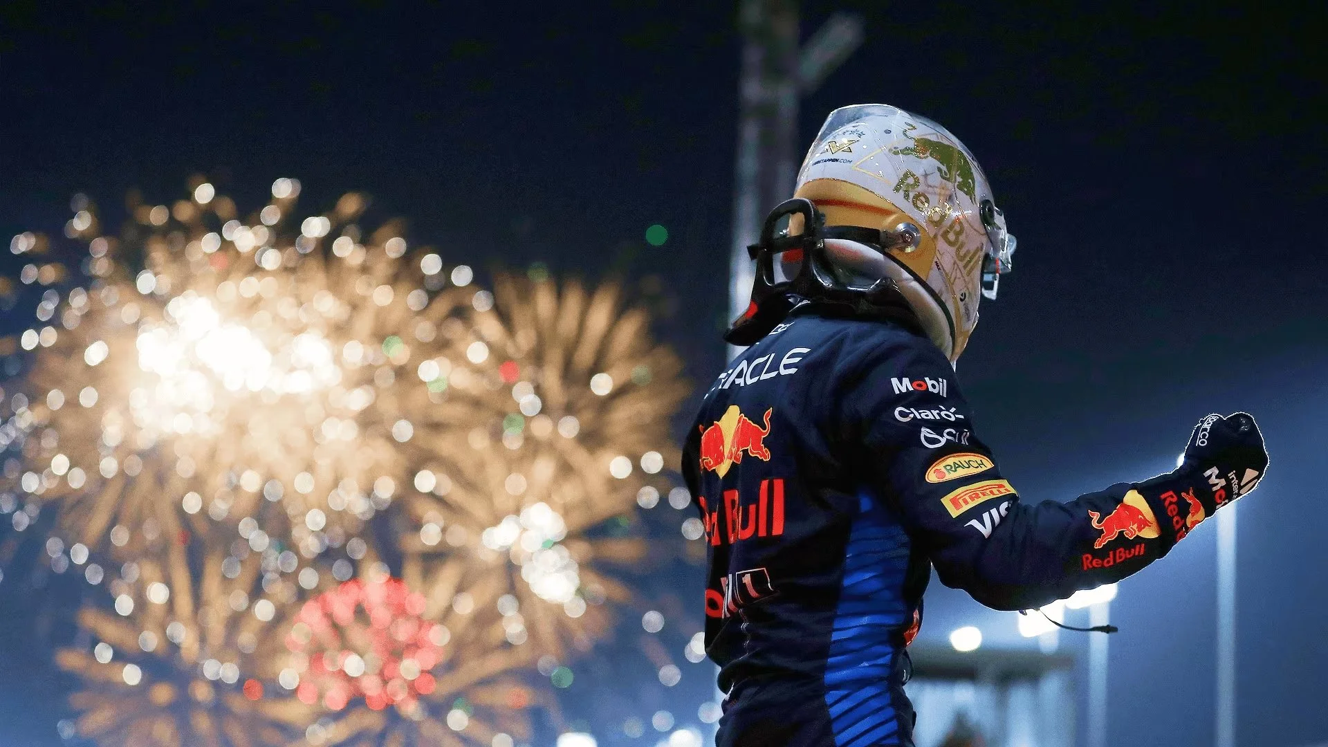 Race car driver celebrating after a race at night, with fireworks in the background.