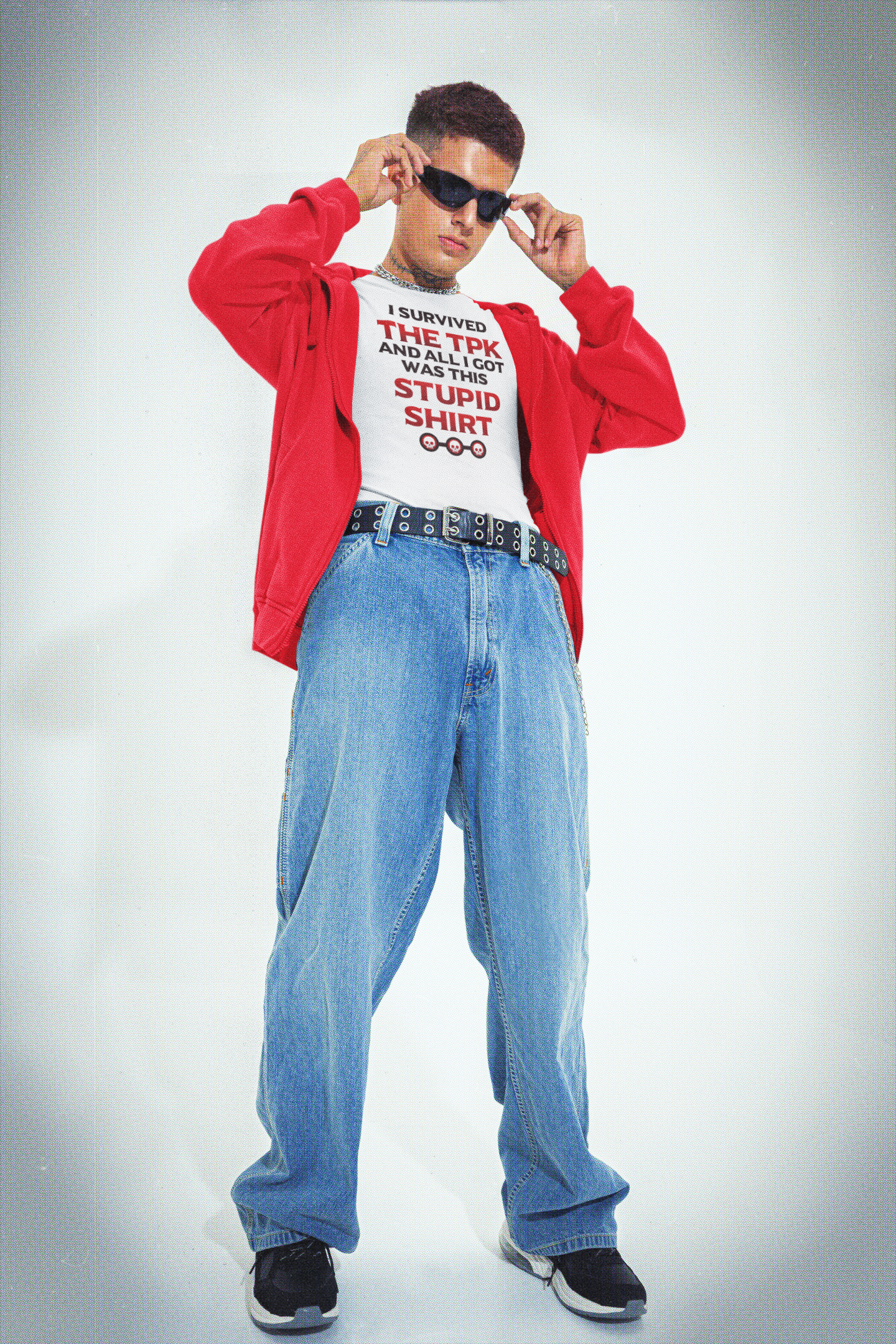 A young man with short dark hair and tattoos on his neck, wearing sunglasses, a white T-shirt with red and black text, a red jacket, baggy blue jeans, and black sneakers with white soles, standing against a light gray background.