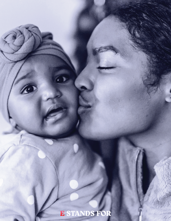 A woman kissing a young girl on the cheek, who is wearing a headwrap and polka-dot shirt, in a close-up black and white photo.