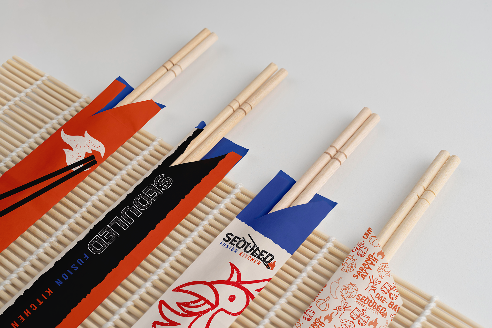 Assorted chopsticks in colorful paper sleeves on bamboo place mat against a white background.