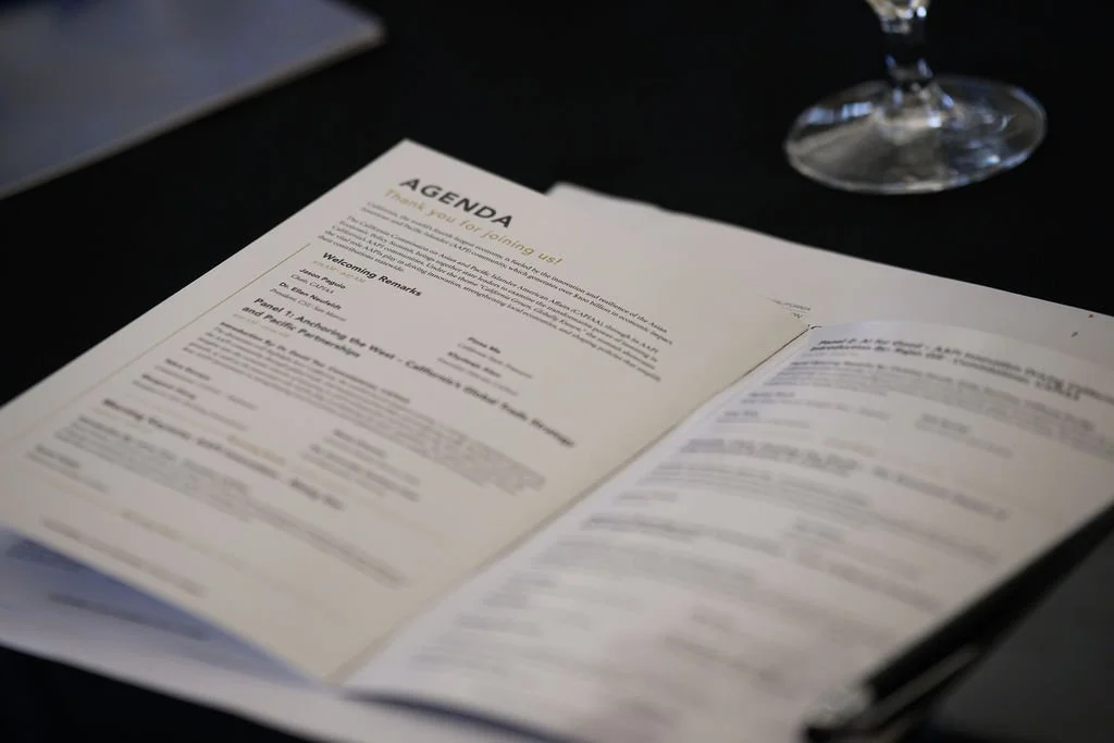 Open agenda or program booklet with the title 'AGENDA' on top, placed on a black table, alongside a glass of water.
