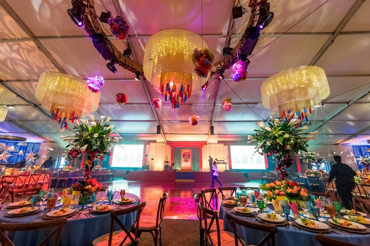 An indoor event decorated with large hanging custom fabric chandeliers, floral arrangements, and colorful lighting.