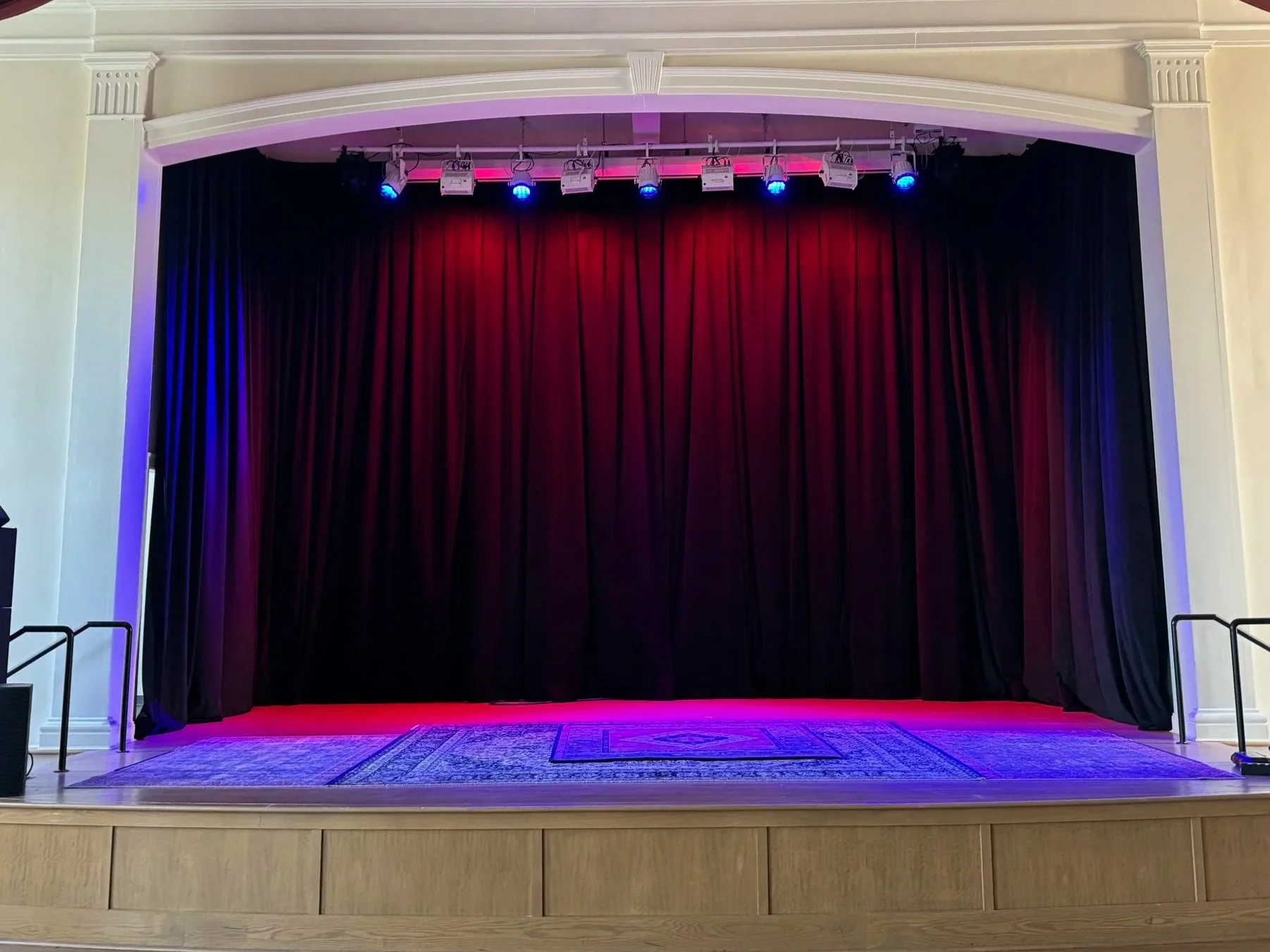 Stage with black curtains, illuminated with blue and pink stage lights. Theatre space with custom drapes.