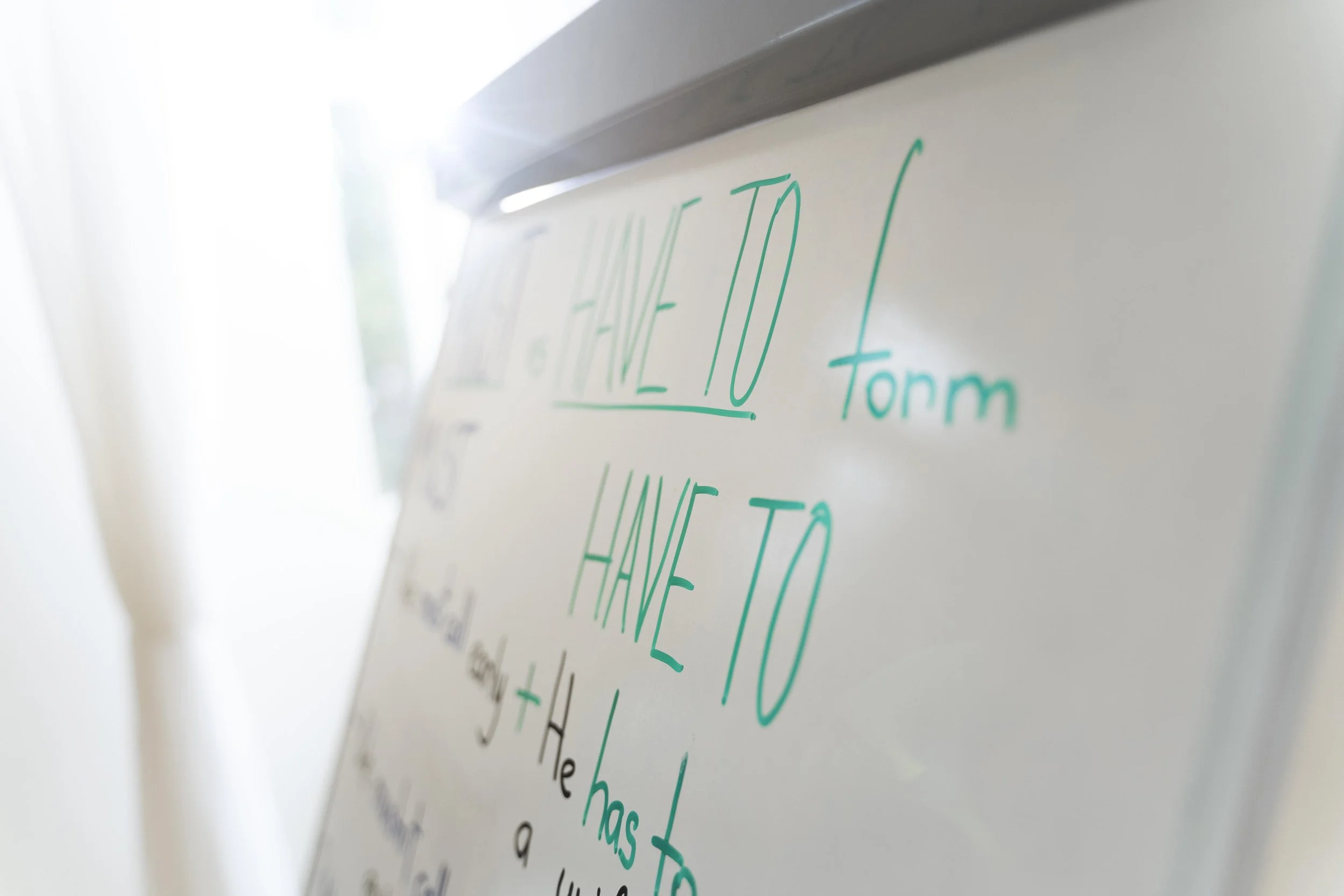 Close-up of a whiteboard with green handwritten text, partially visible, with sunlight causing glare on the top left corner.