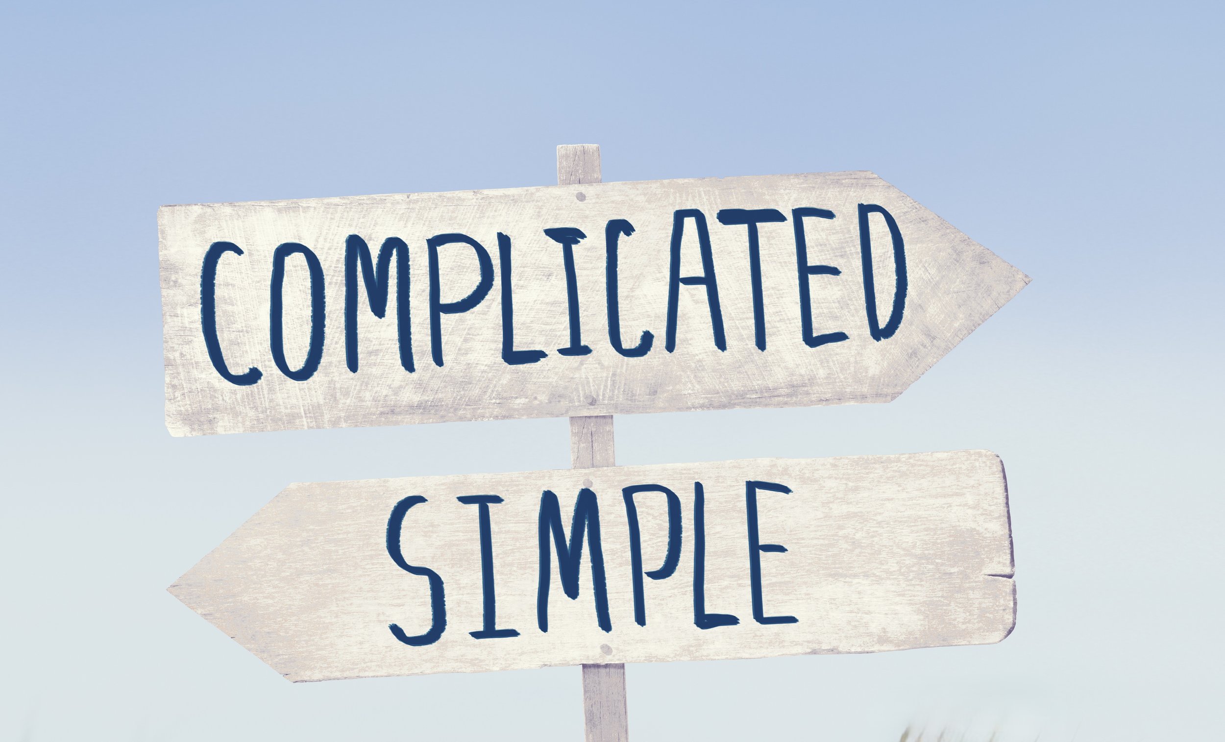 Wooden directional sign with the words "COMPLEATED" and "SAMPLE" written in blue paint, pointing to nearby locations, against a clear blue sky.