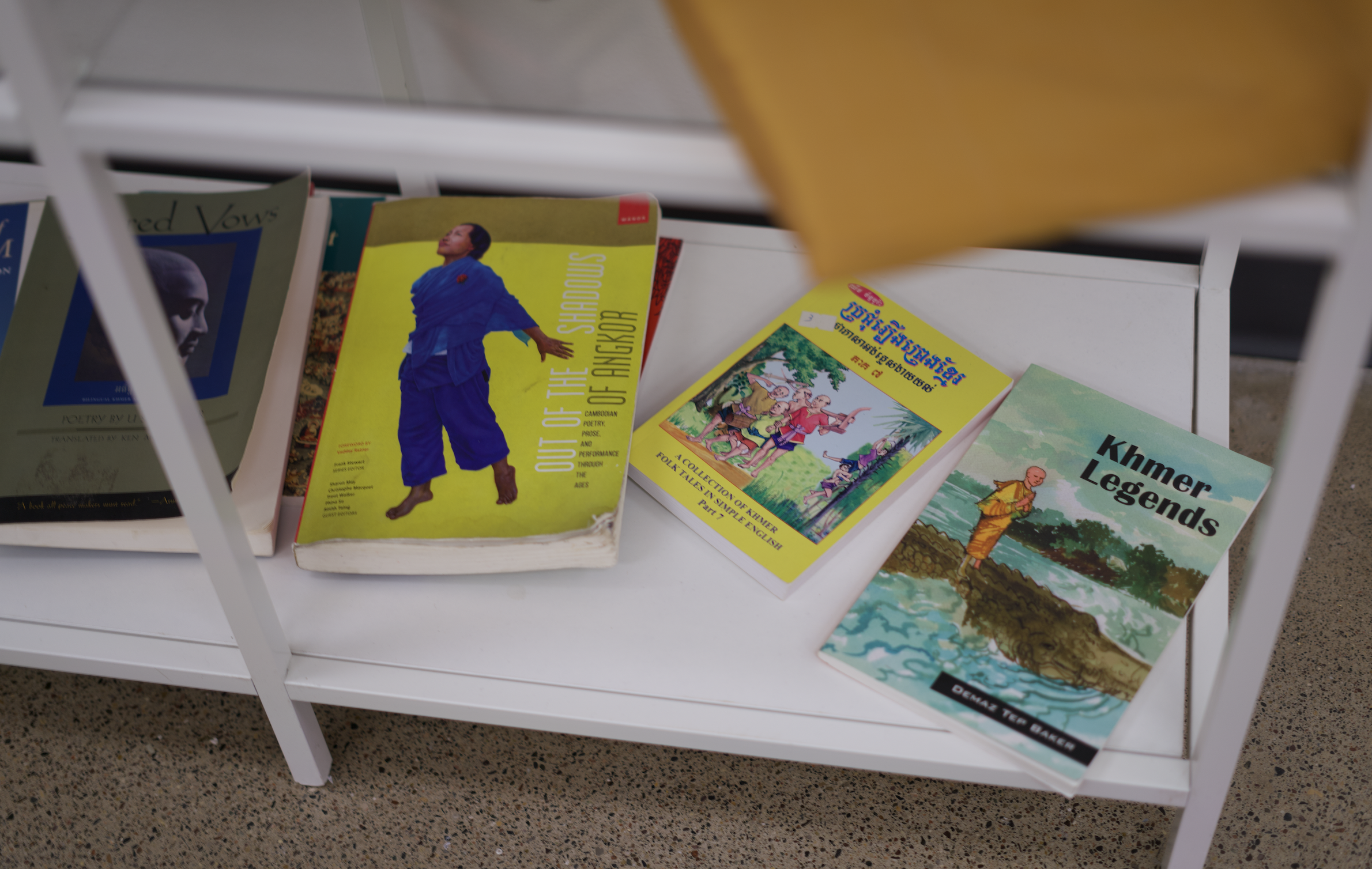 Books on a white shelf, including titles about Khmer legends, Khmer folklore, and a book with a person dressed in traditional attire on the cover, with other books featuring portraits and landscapes.