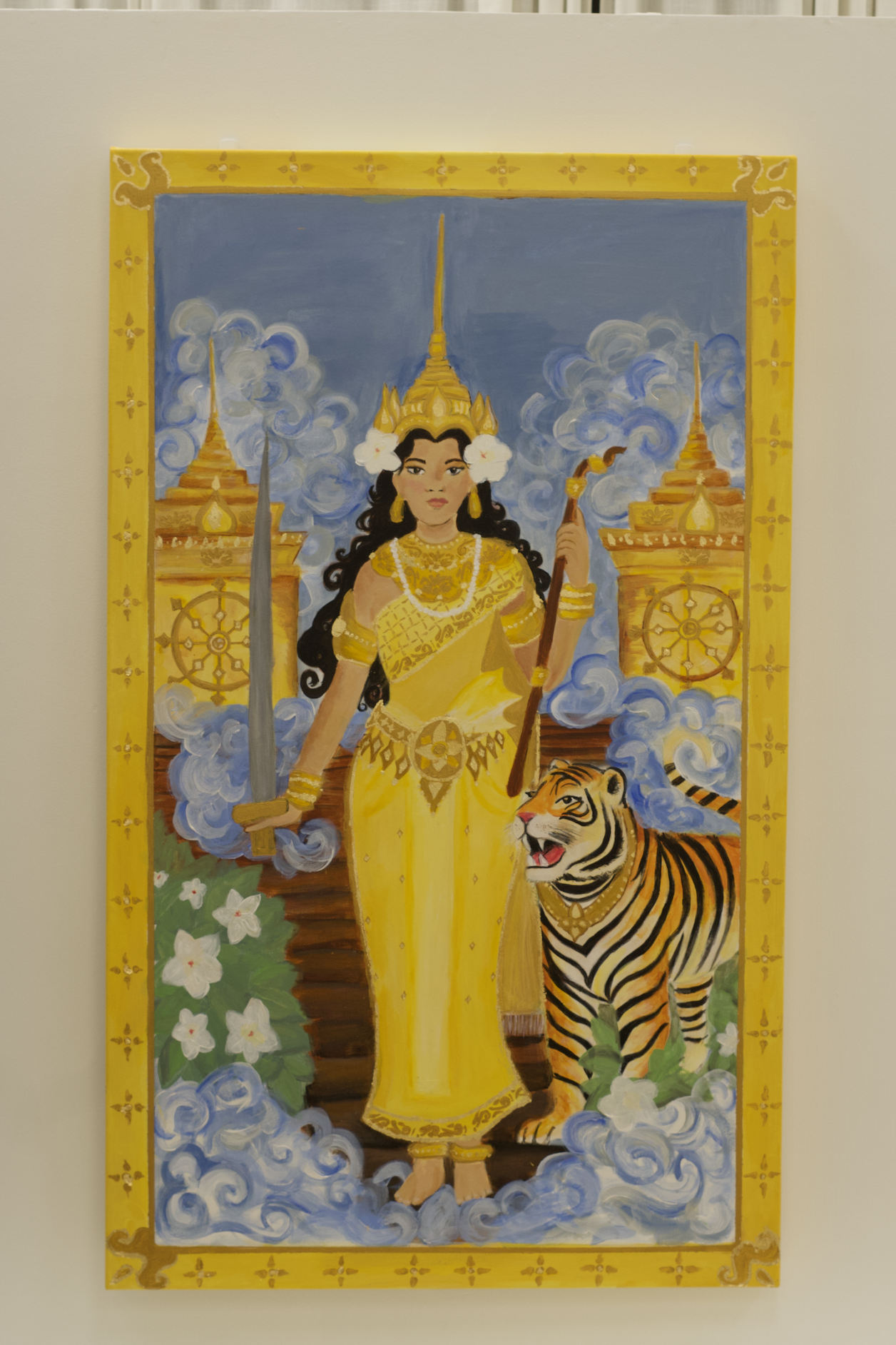 Painting of a woman in traditional Southeast Asian attire with a tiger, set against a backdrop of clouds and golden temple structures, framed in yellow with decorative patterns.
