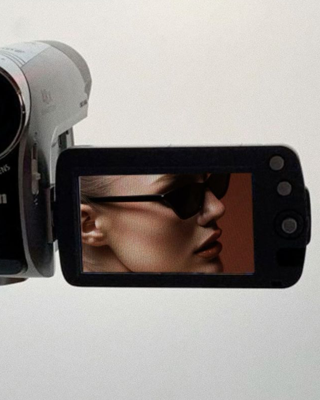 The camera's display shows a woman wearing sunglasses with a close-up profile view of her face.