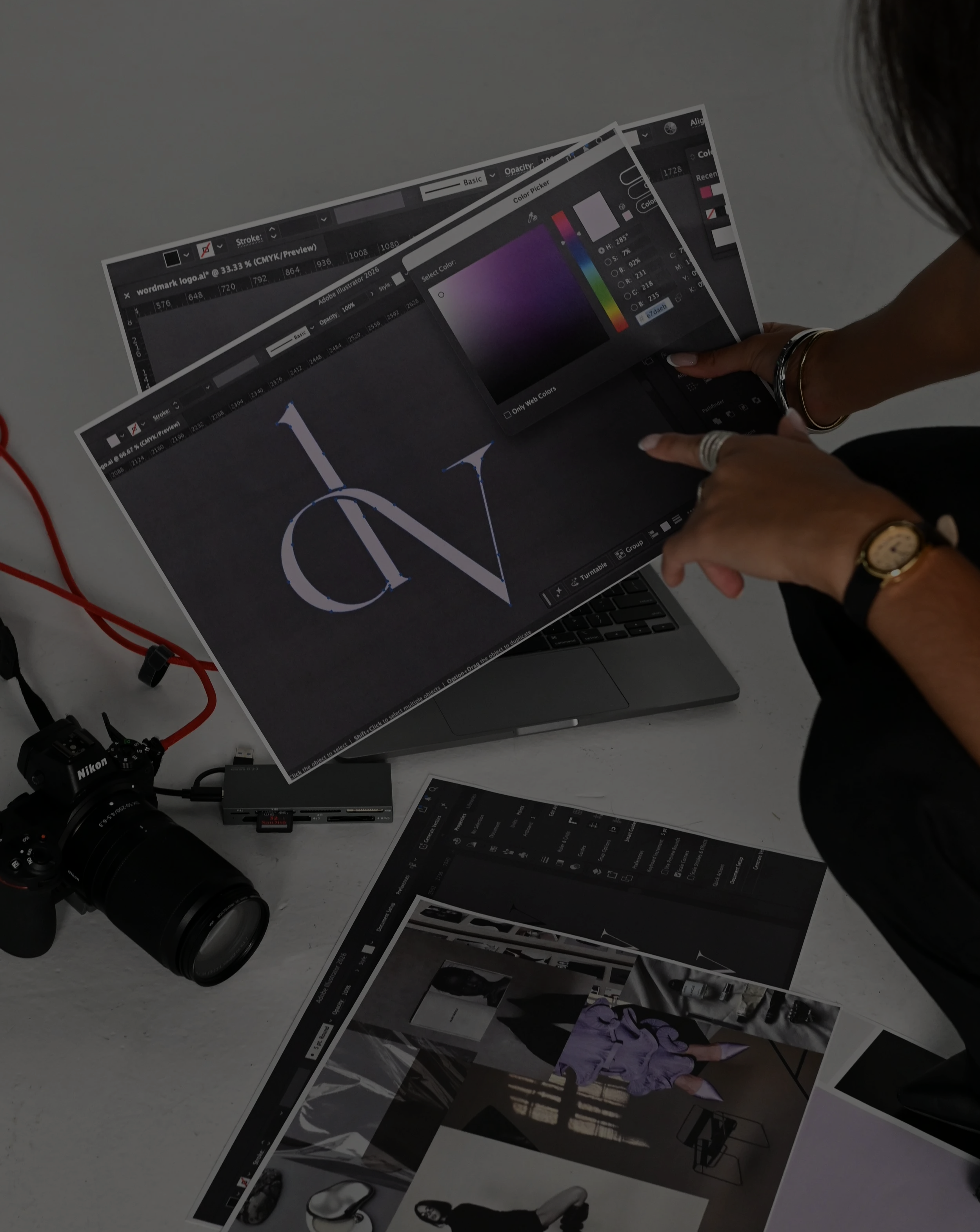Several printed photographs of fashion models and a camera on a white surface, with some electronic equipment and cables nearby.
