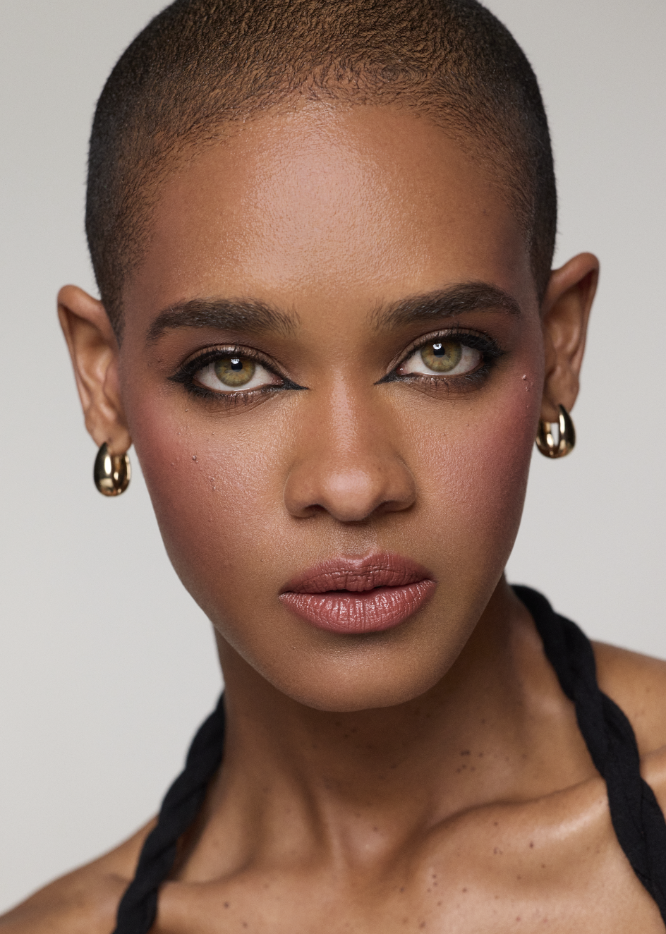 Close-up portrait of a woman with short hair, gold hoop earrings, and makeup, looking directly at the camera.
