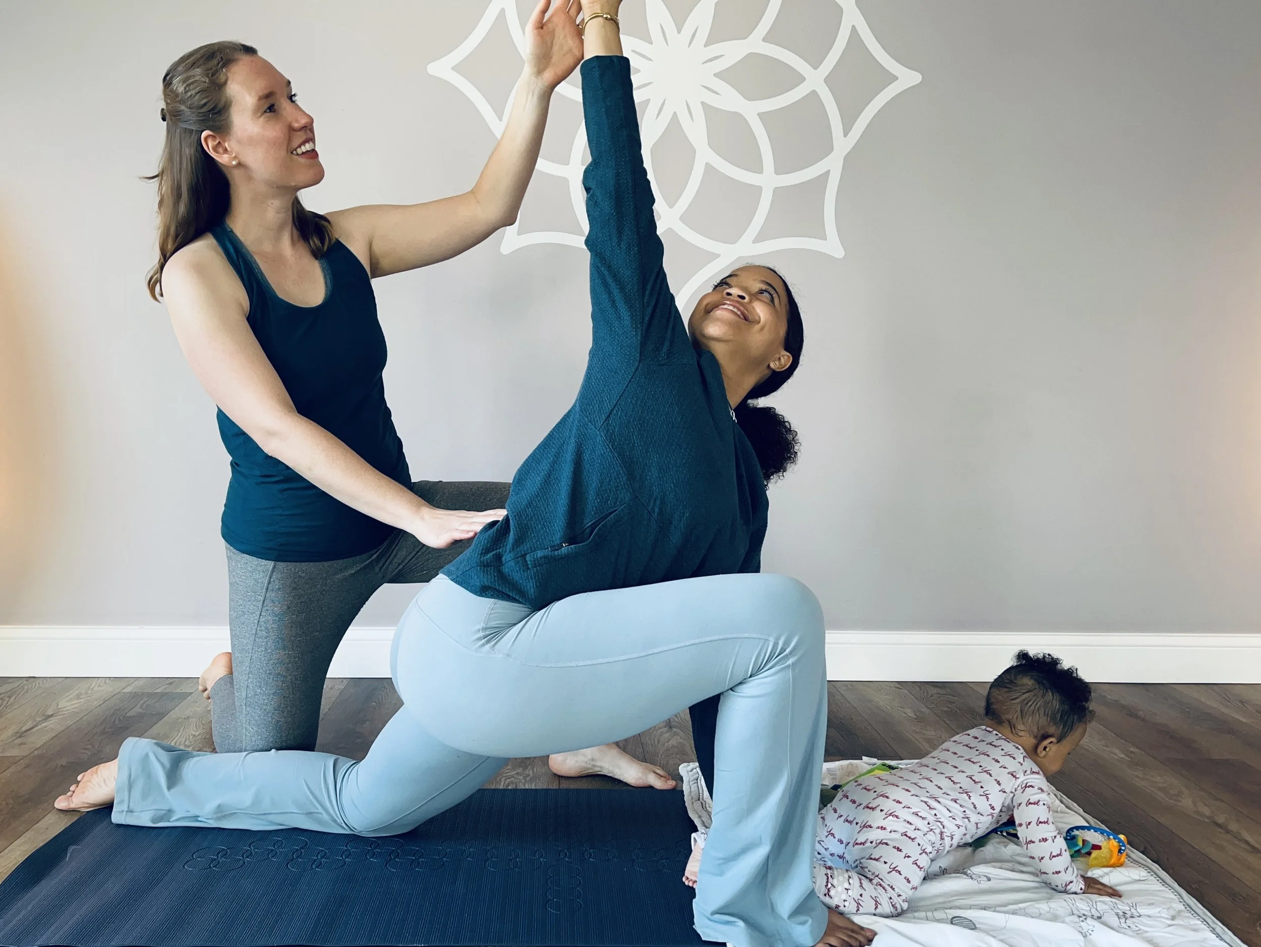 pelvic floor physical therapist assists a postpartum patient with a stretch while the patient's baby plays on the floor