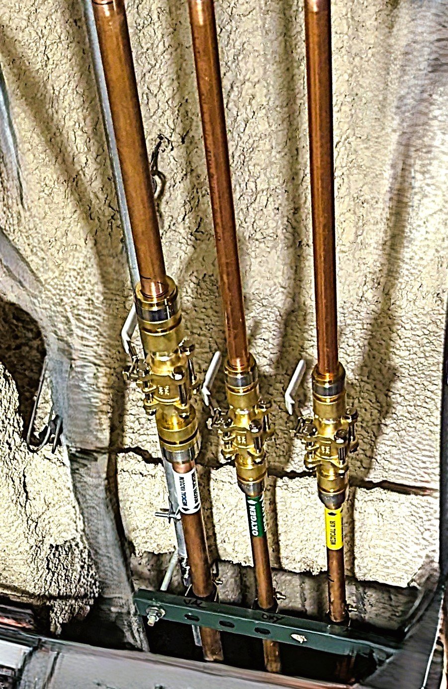 Three copper water supply lines connected to brass shut-off valves mounted on a wall with drywall behind.