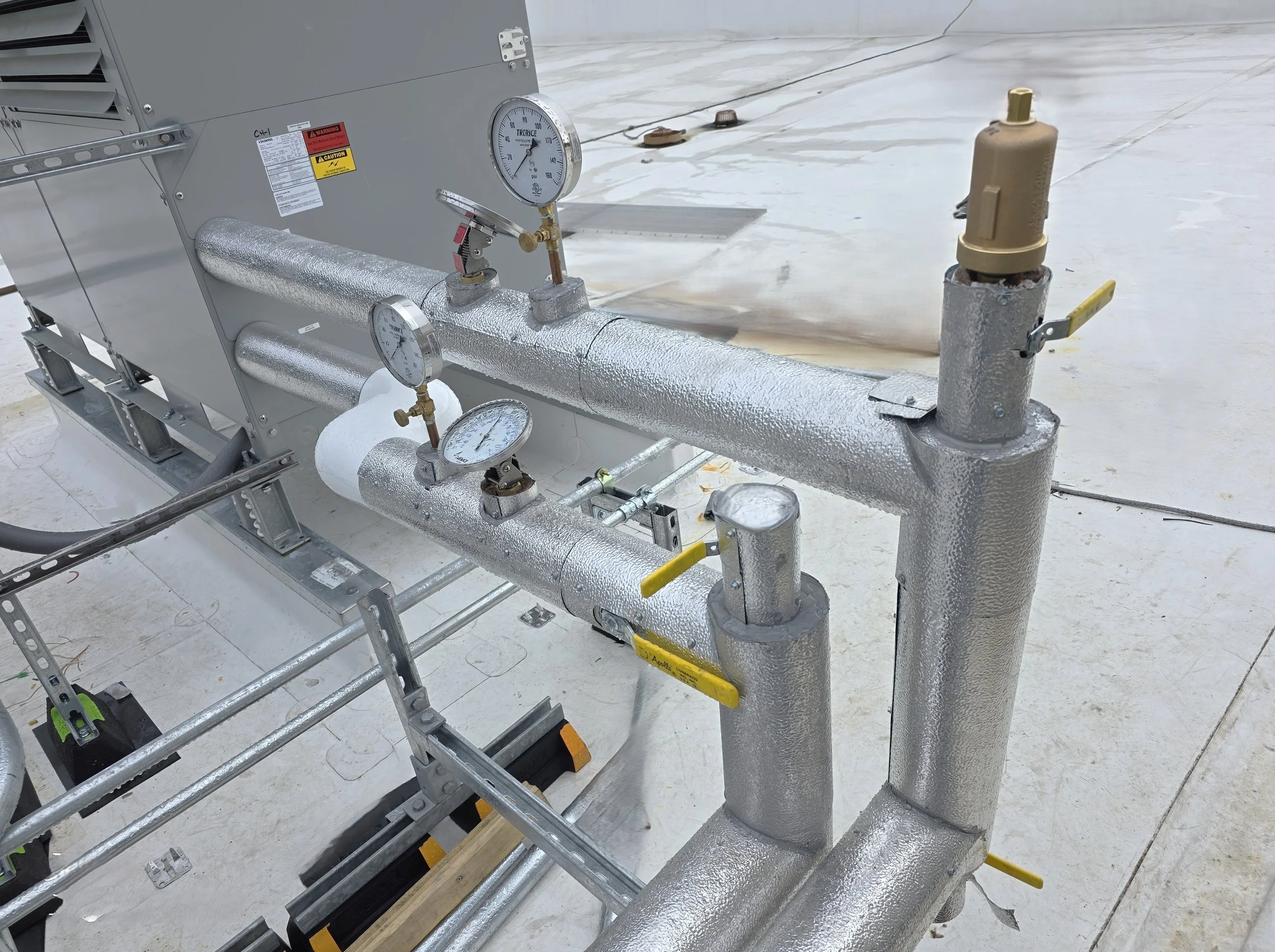 Industrial pipes wrapped in insulation on a white floor with gauges and valves.