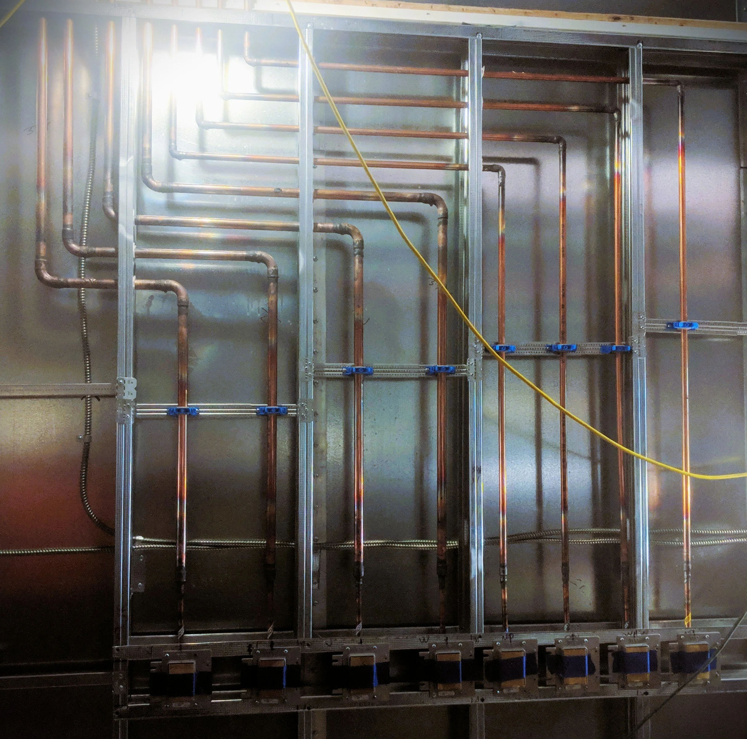 Interior of a building under construction with metal framing, copper piping, and electrical conduits installed on the walls.