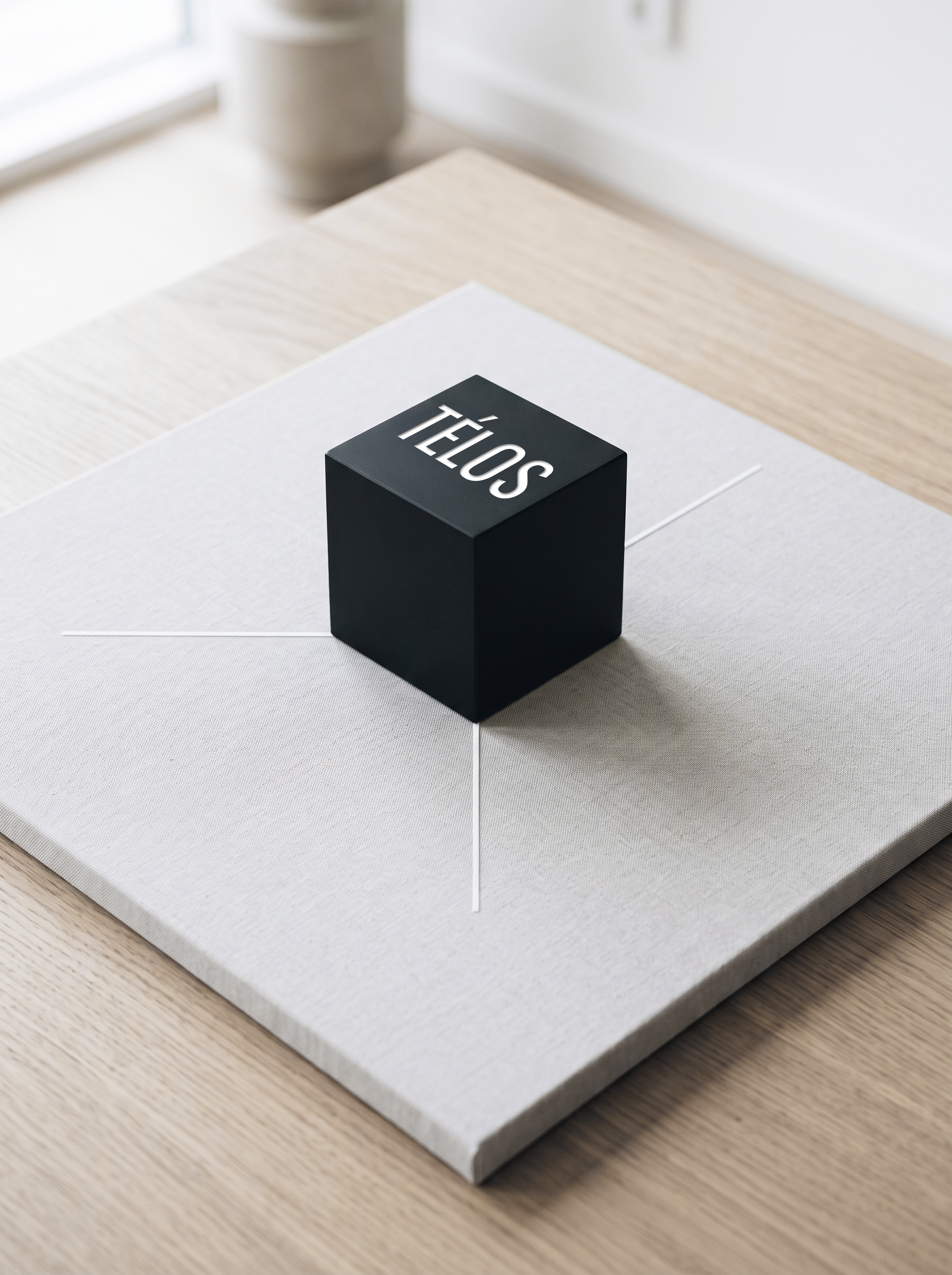 Caja negra con la palabra 'TELÓS' escrita en letras blancas, colocada sobre una mesa con mantel claro.