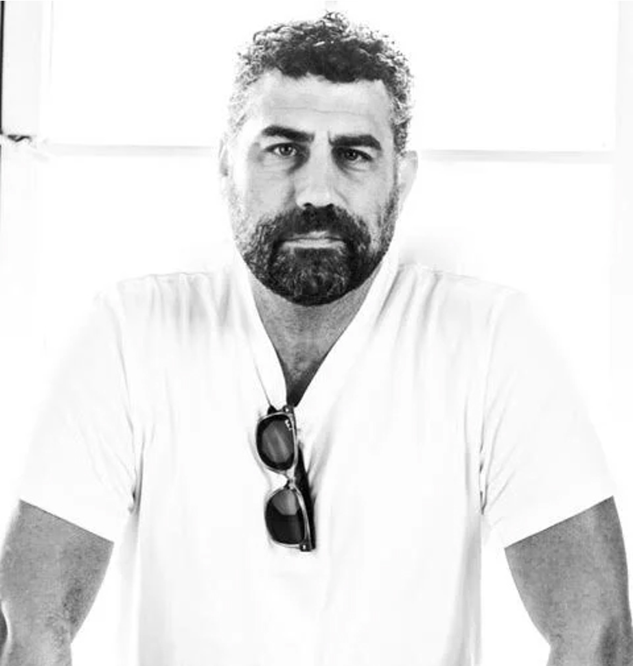 A black and white photo of Rob Farber with dark, curly hair and a beard, wearing a white t-shirt and sunglasses hanging from his neck, looking directly at the camera.