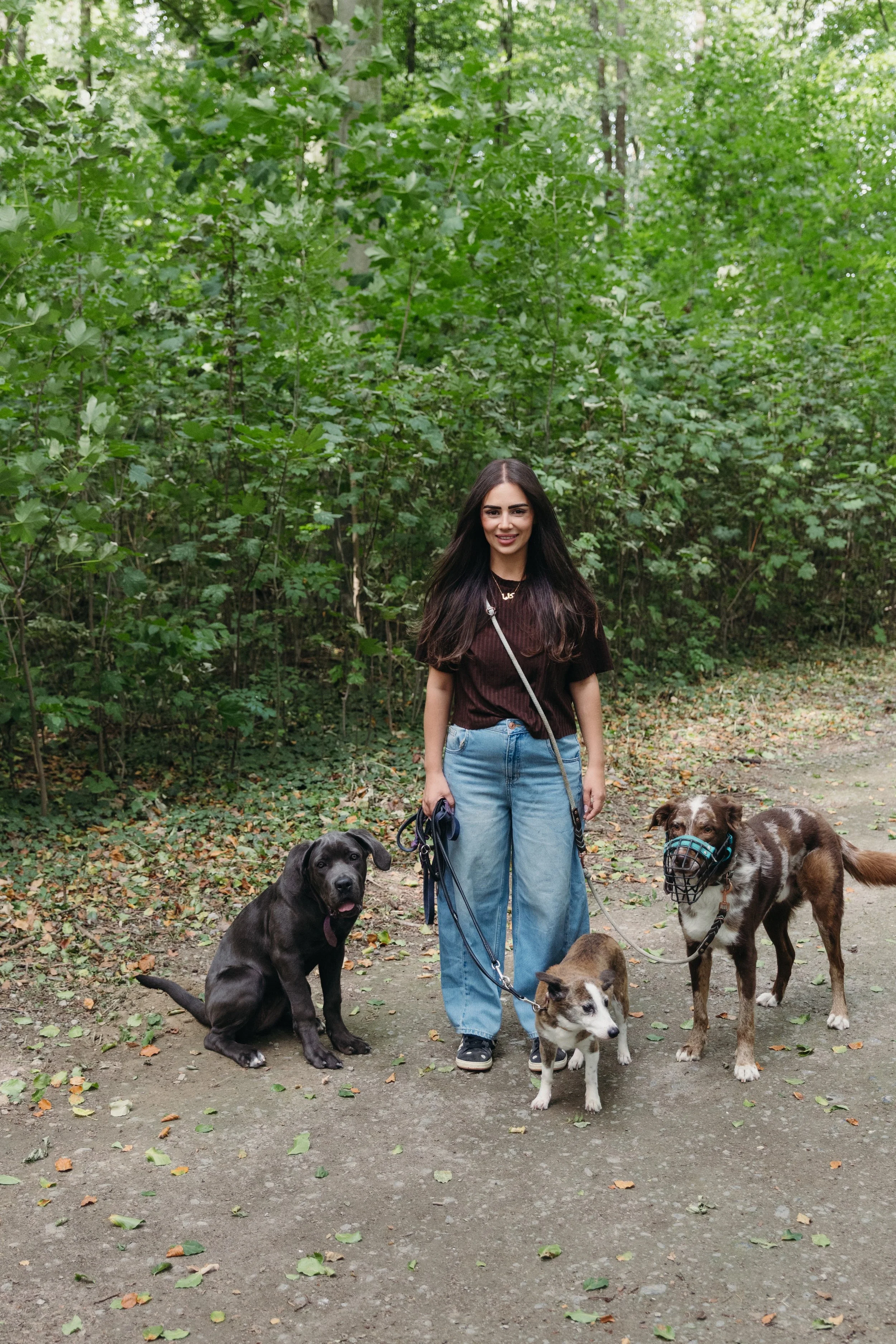 Hundetrainerin Natascha steht lächelnd mit ihren drei Hunden an der Leine auf einem Waldweg in Soest