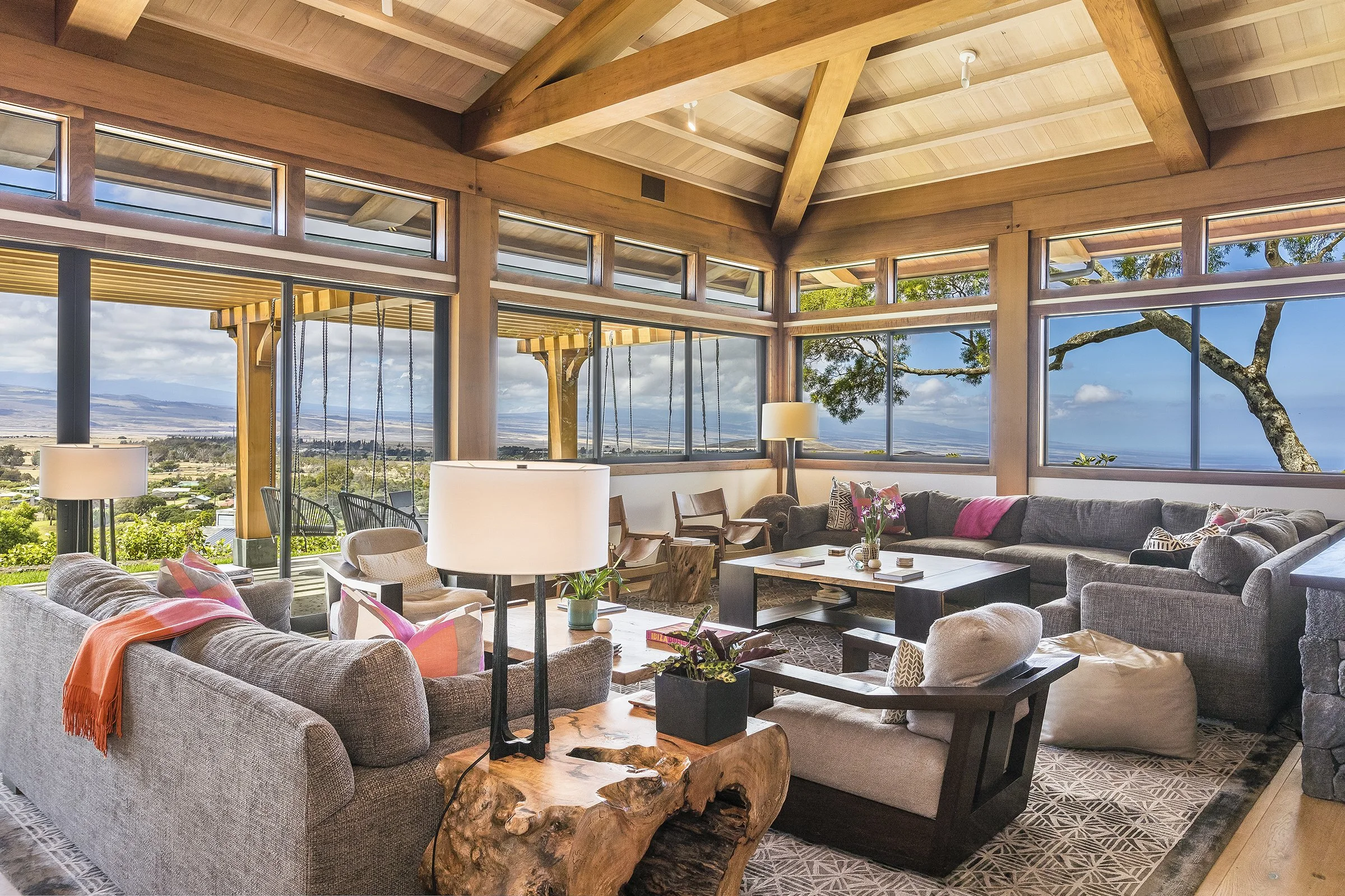 Living room with large windows, grey and beige sofas, wooden coffee table, and outdoor scenery including trees and landscape.