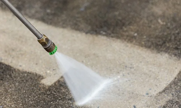 A pressure washer nozzle spraying water on an asphalt surface.