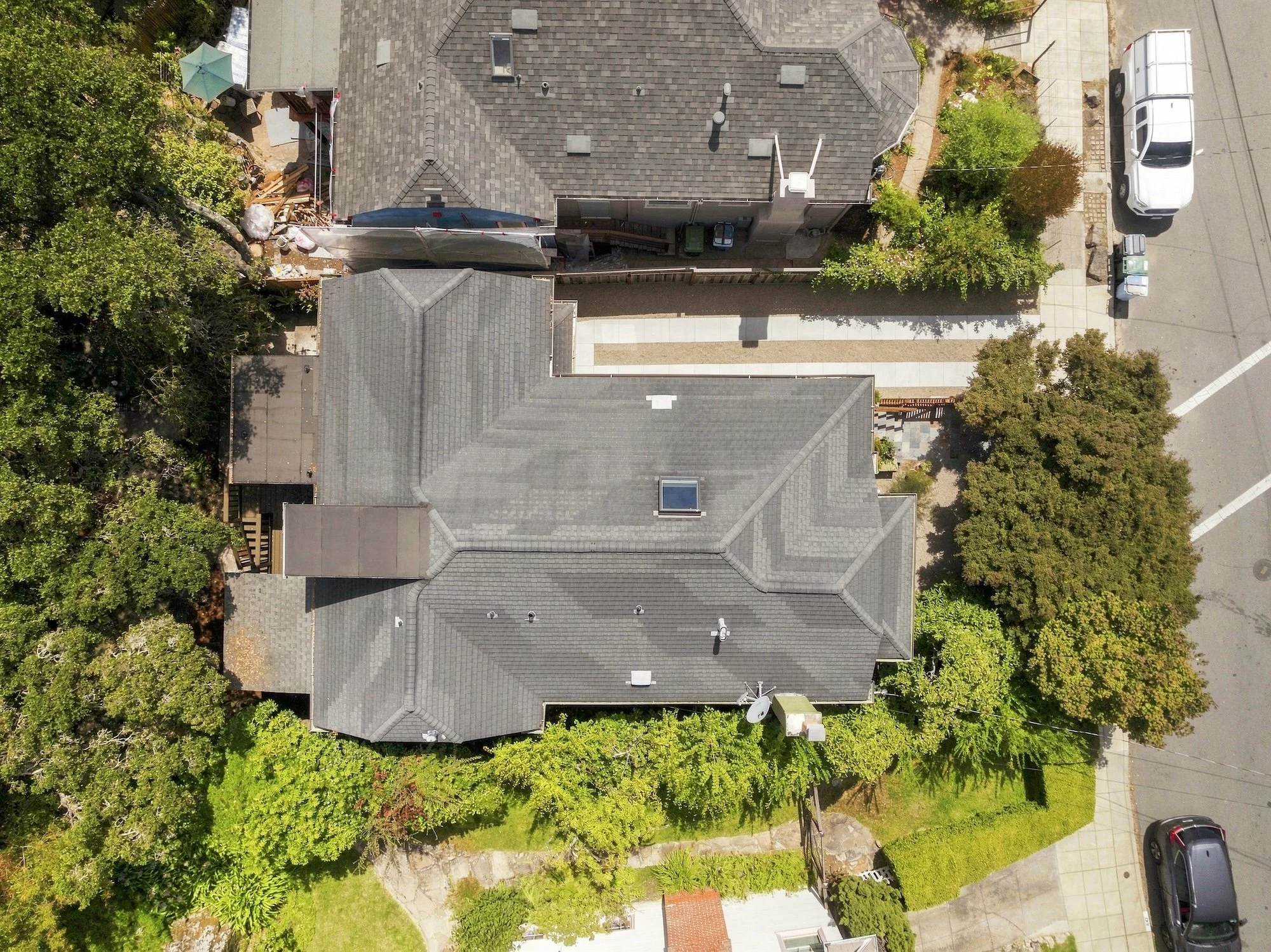 Aerial view of residential houses with gray roofs, trees, parked cars, and a construction site with a tarp and wooden planks.