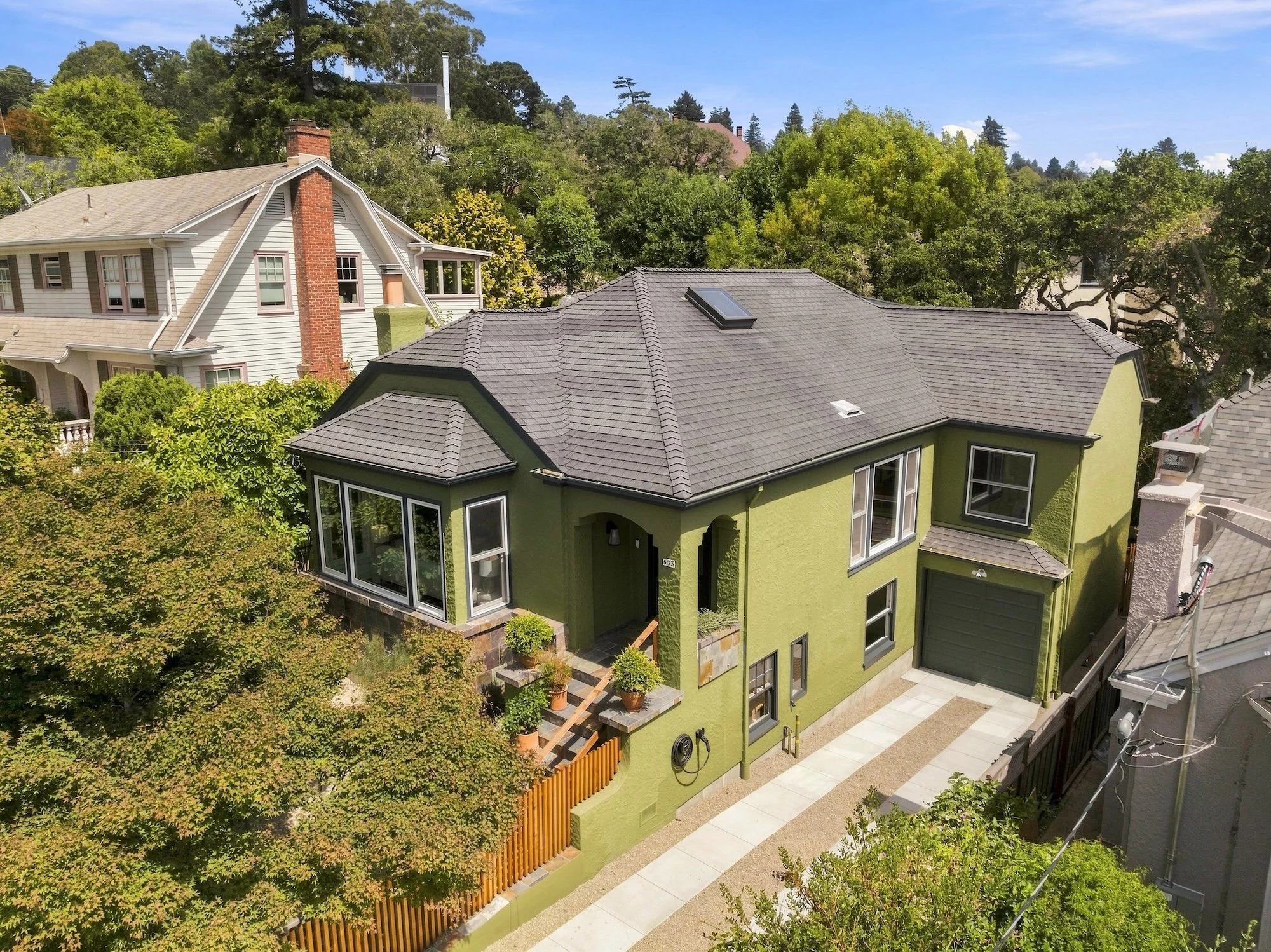 Aerial view of three houses with different color schemes, surrounded by trees and greenery under a clear blue sky.