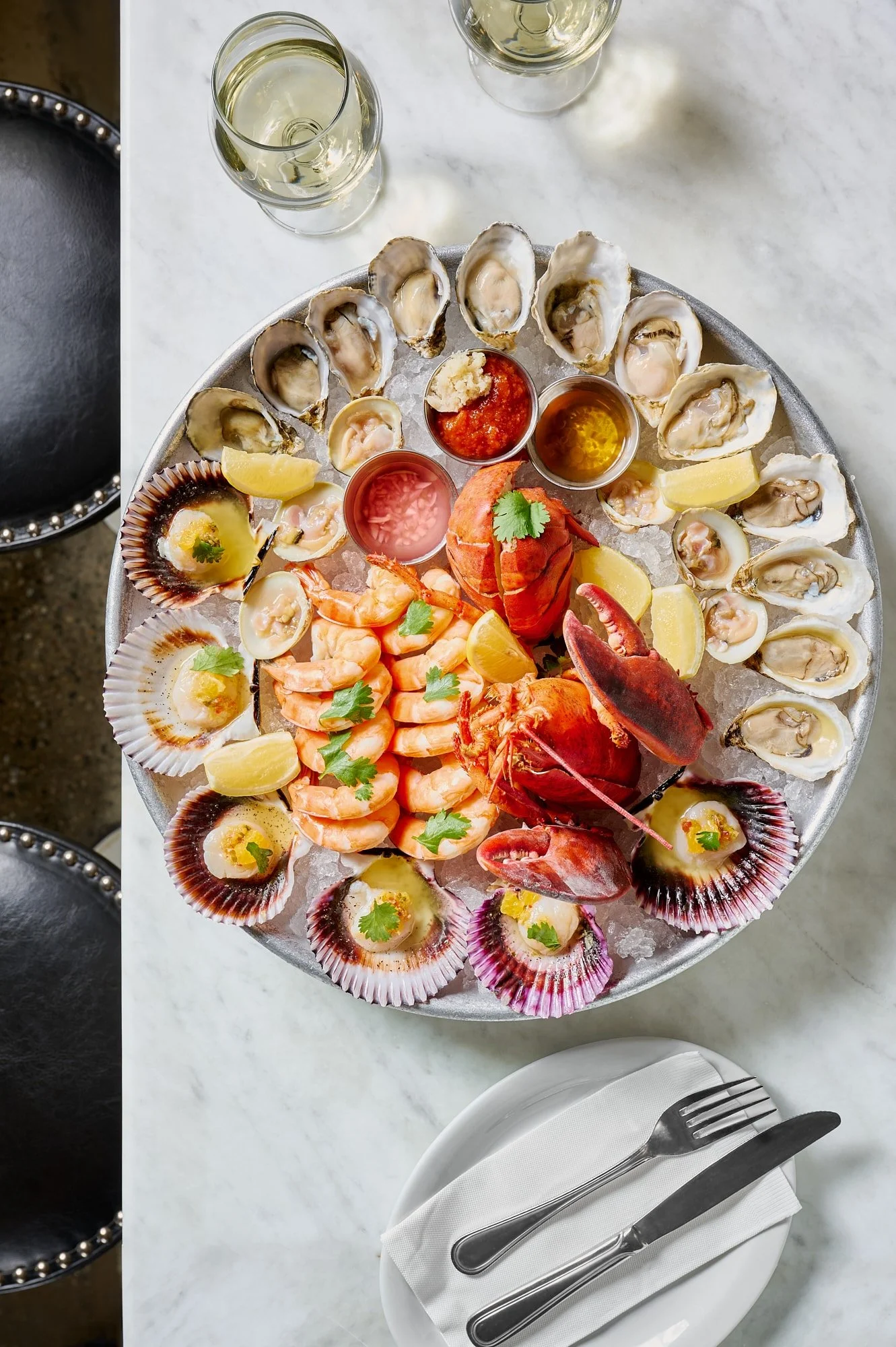 Overhead shot of a seafood platter with oysters, clams, shrimp, and lobster served with lemon and sauces.