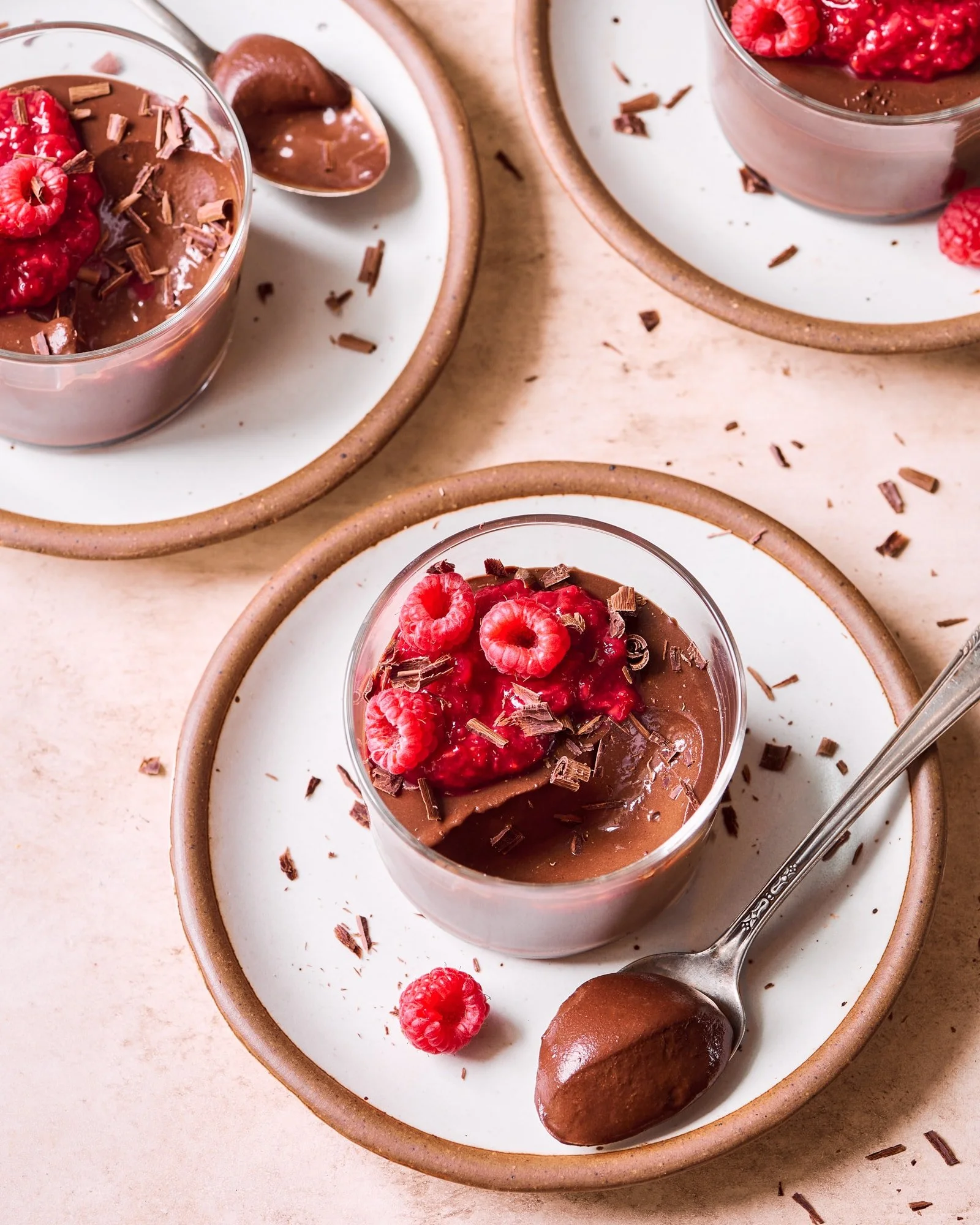 Chocolate mousse topped with raspberries, chocolate shavings, and a brownie on a white plate with a brown rim.