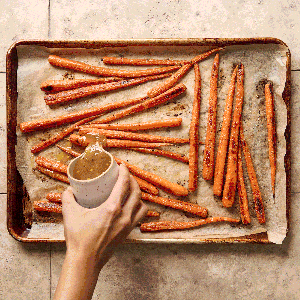 Roasted carrots on a baking sheet being drizzled with sauce.