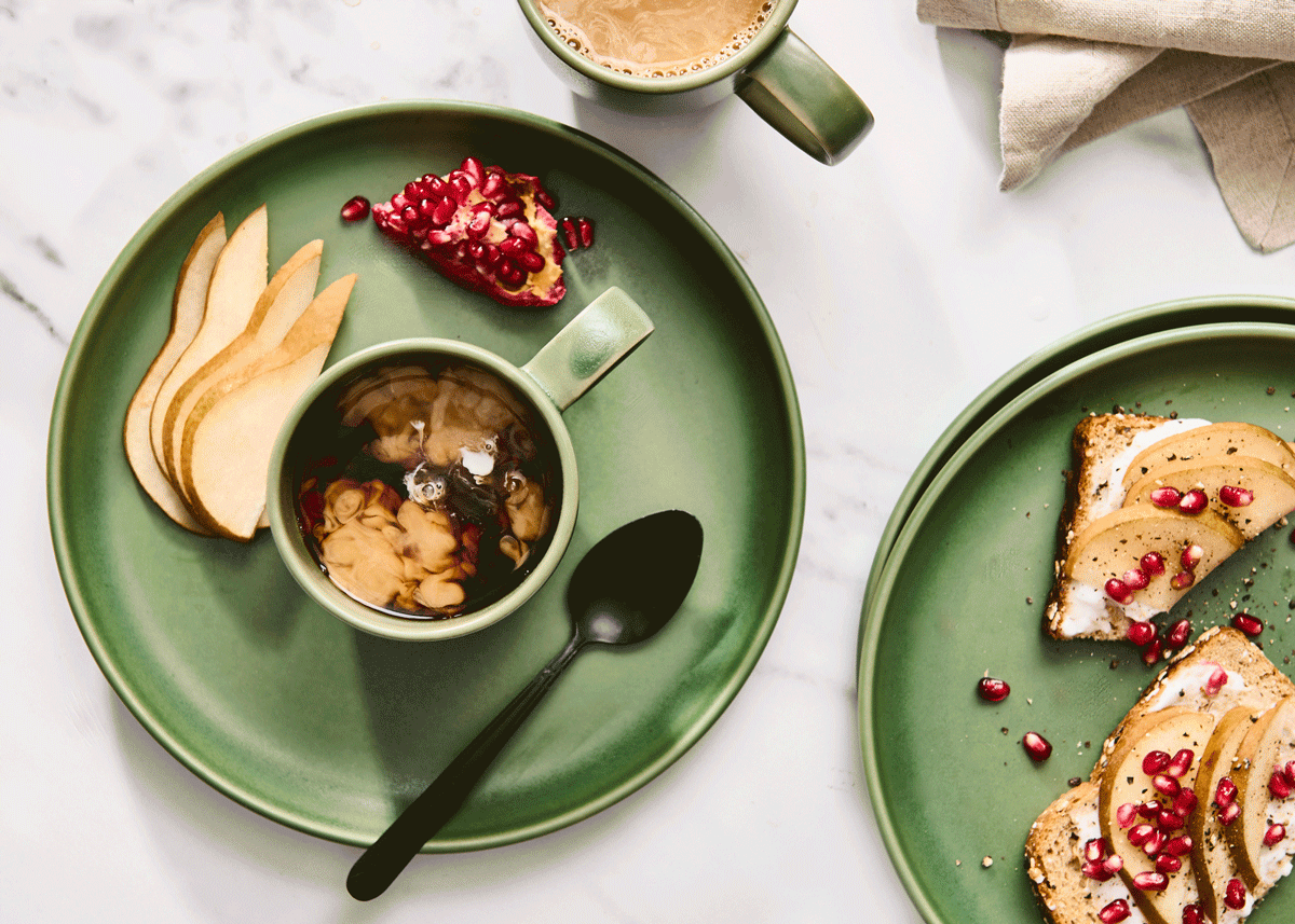 Top-down breakfast spread with oatmeal, sliced pear, pomegranate seeds, toast, and coffee on green plates