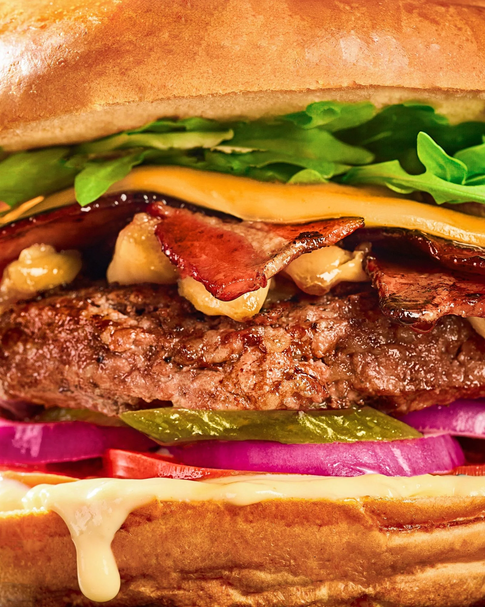 Close-up of a cheeseburger with a beef patty, melted cheese, bacon, lettuce, pickles, onions, and tomato on a toasted bun
