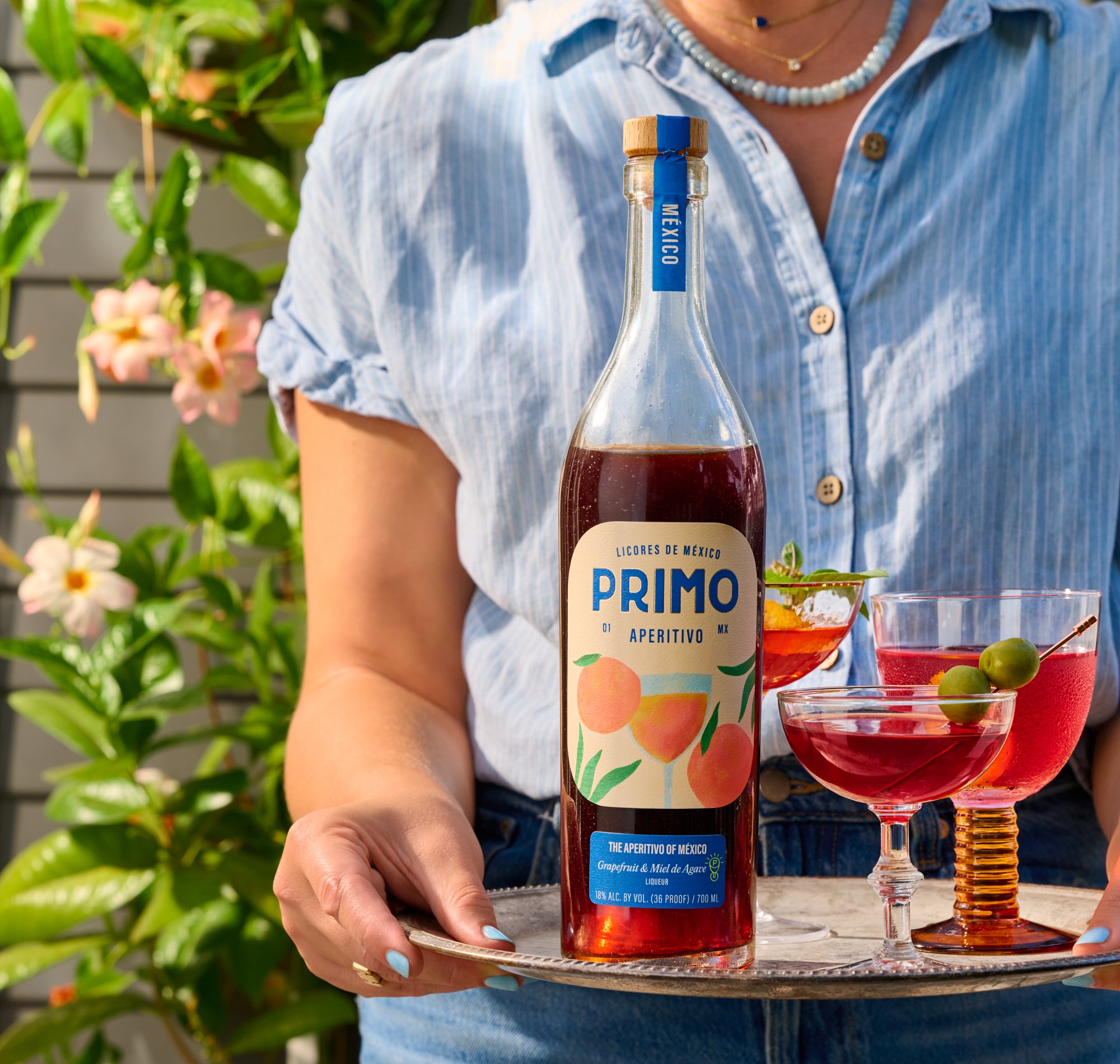 Bottle of Primo grapefruit an agave aperitif from Mexico with red cocktails garnished with green olives on a serving tray