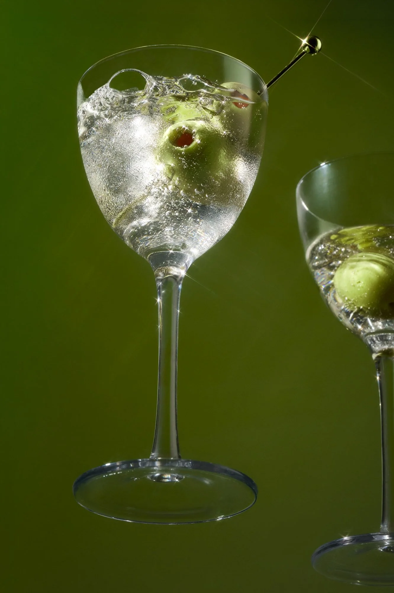 Sparkling cocktails with green olives in martini glasses against a dark green background