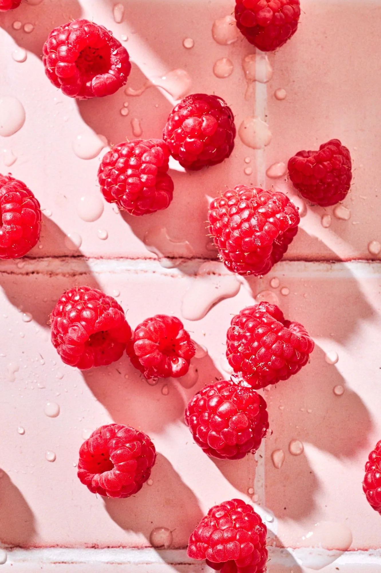 Fresh raspberries with water droplets on light pink surface.