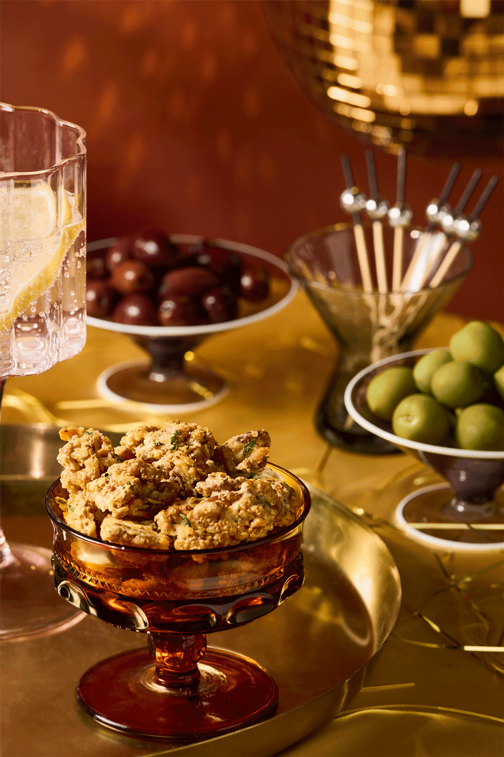 A festive holiday scene with a disco ball, gold table setting and a bowl of rosemary walnuts in the foreground.