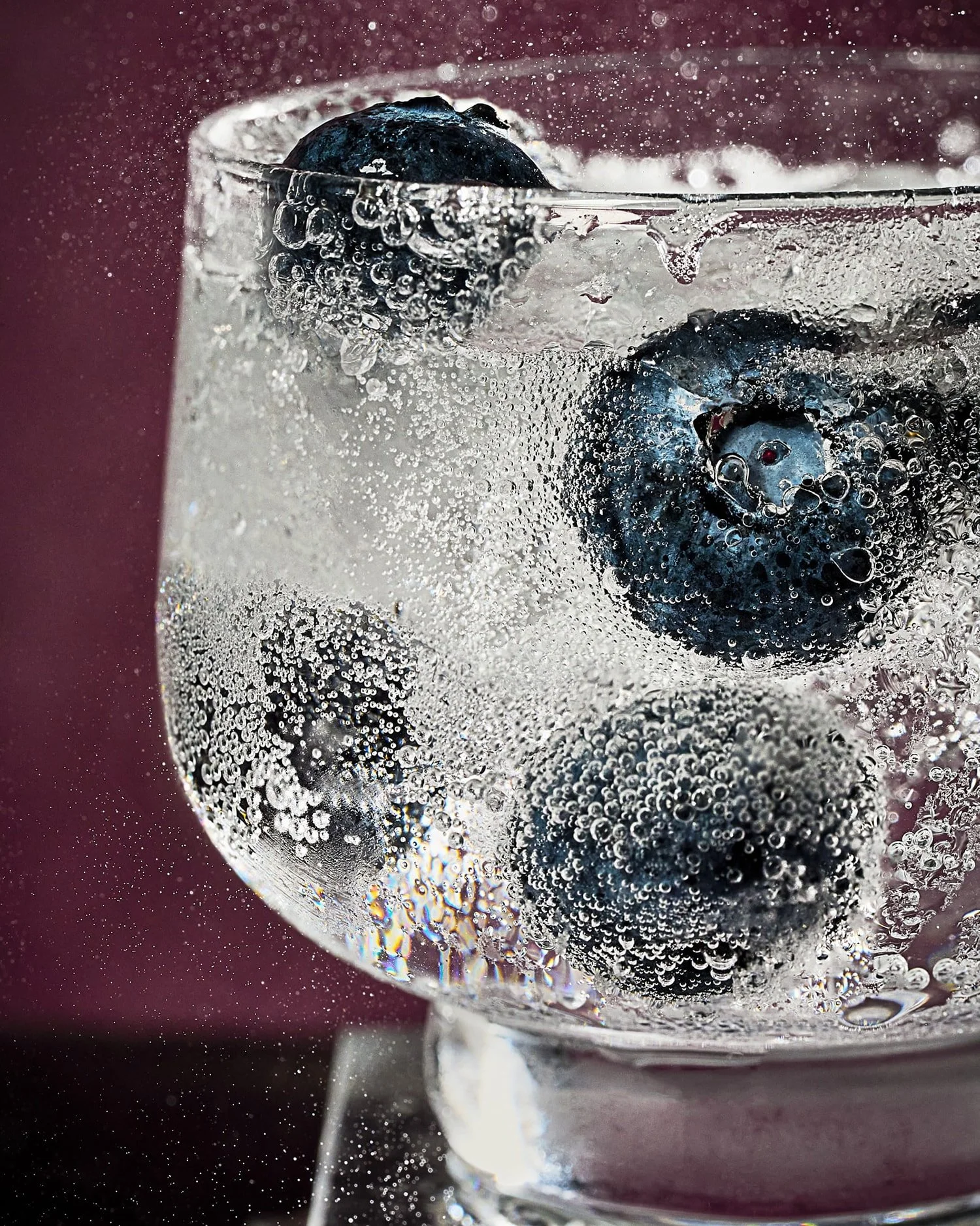 Close-up of blueberries submerged in sparkling water, covered with bubbles in a glass.
