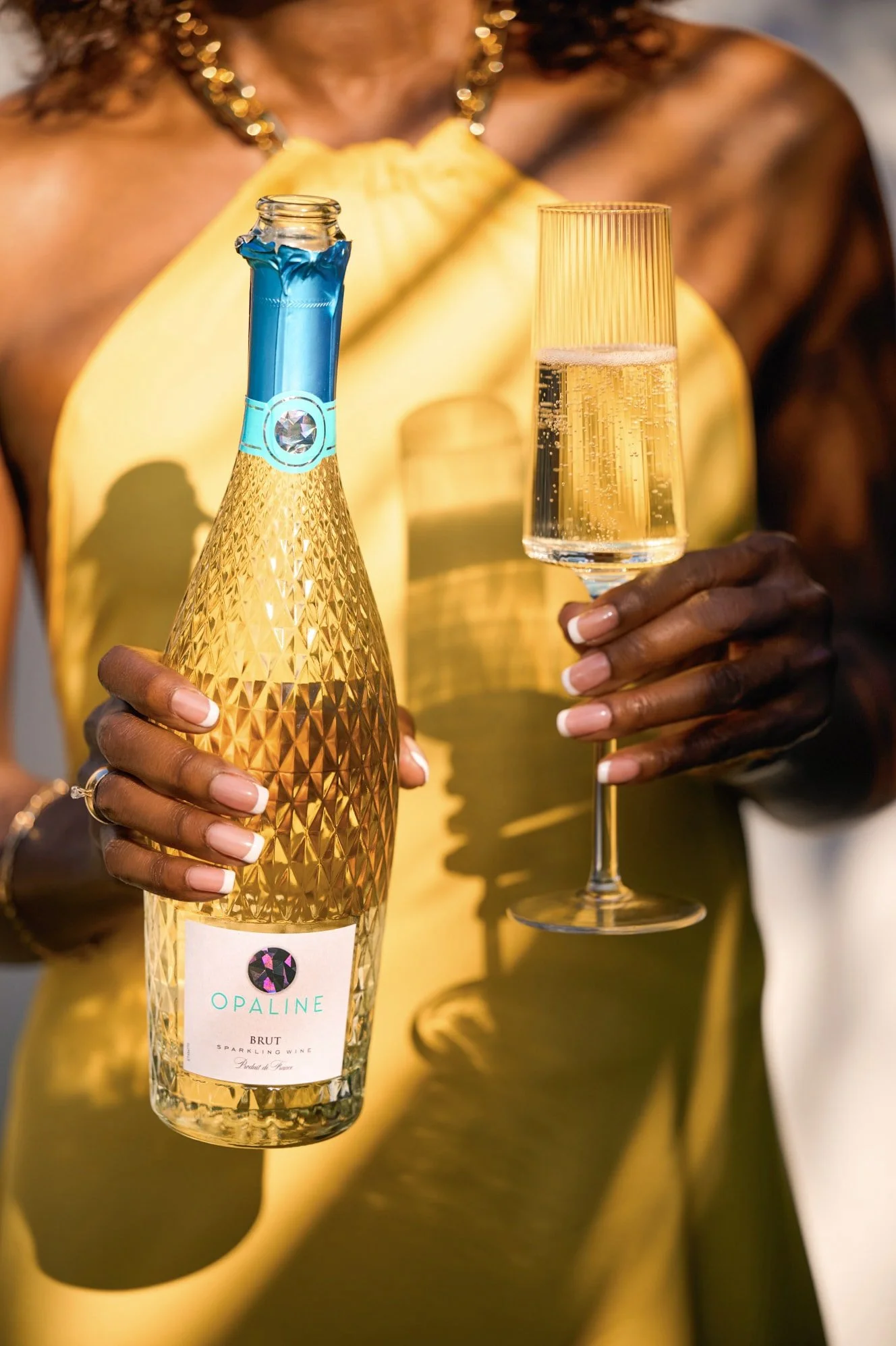 Woman holding a bottle of Opaline Brut sparkling wine and a flute of champagne.