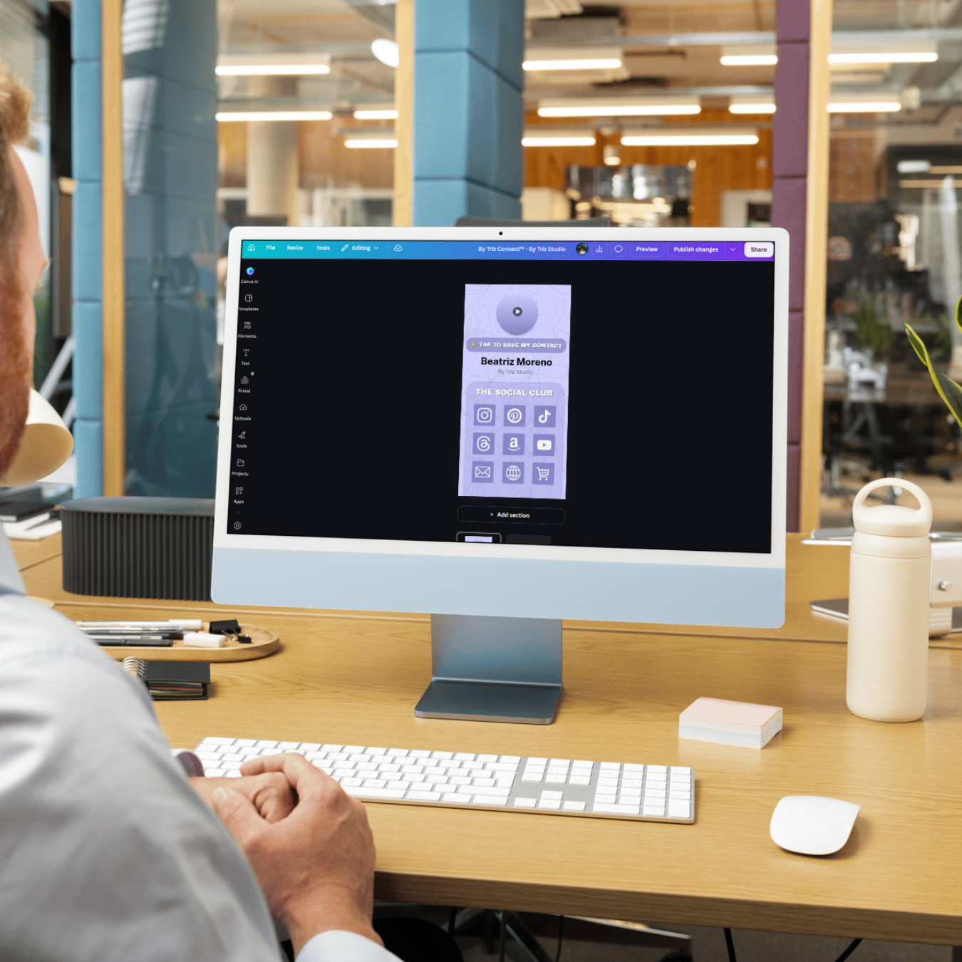 Person working at a desk with an iMac displaying a mobile app design with social media icons and contact options.