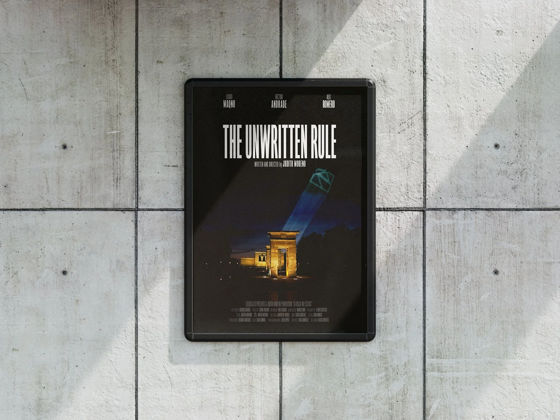 Poster for a film titled 'The Unwritten Rule' featuring imagery of a beam of light shining on an archaeological site at night with trees in the background, mounted on a concrete wall.