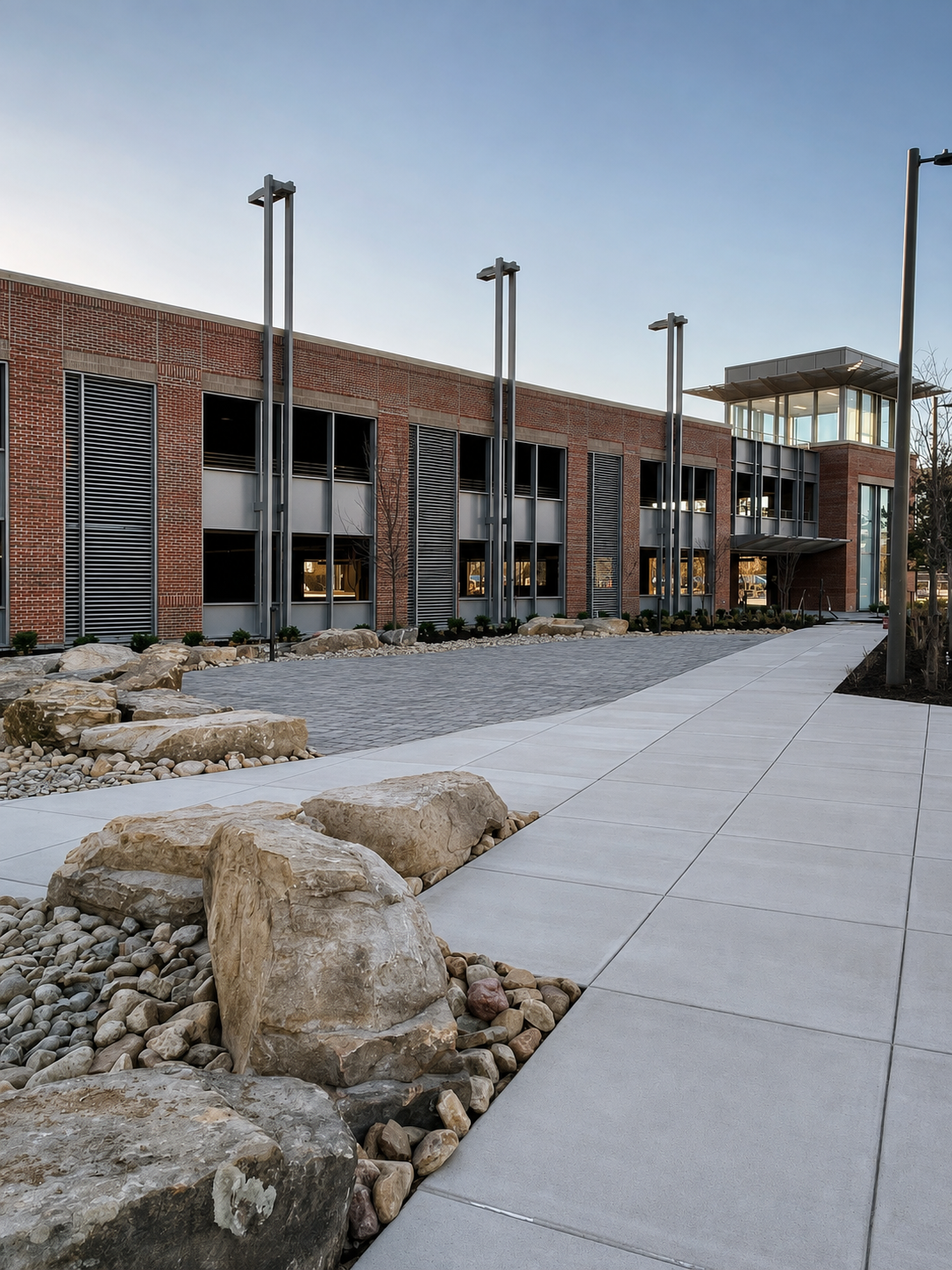 Modern building with brick and glass exterior, stone landscaping, and a paved walkway.