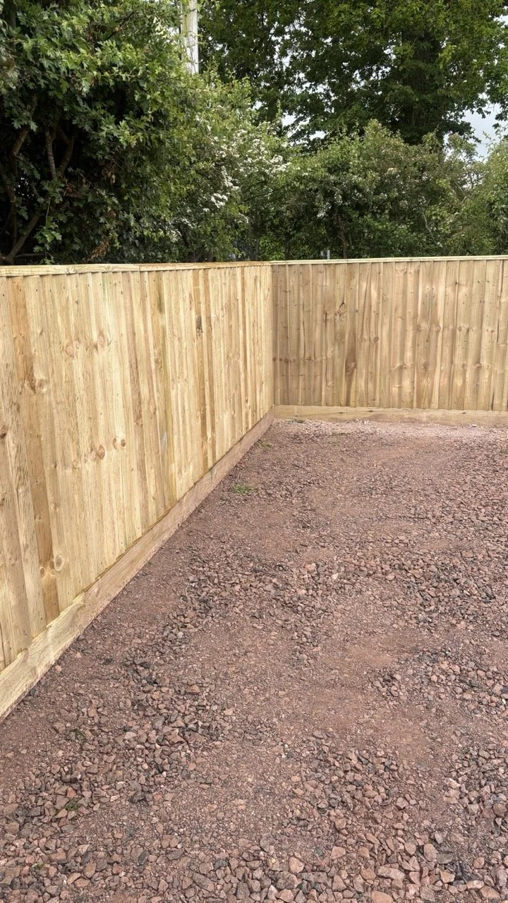 A new wooden privacy fence with a gravel ground in front and trees in the background.