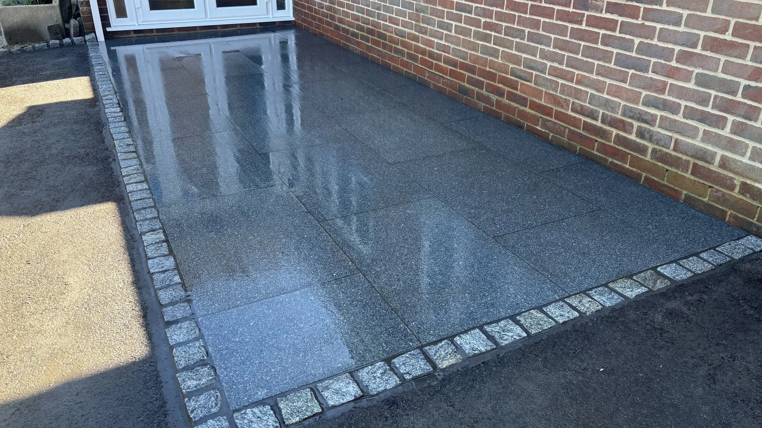 A freshly cleaned front porch with black tile flooring surrounded by decorative stone border, adjacent to a brick wall and a white door.