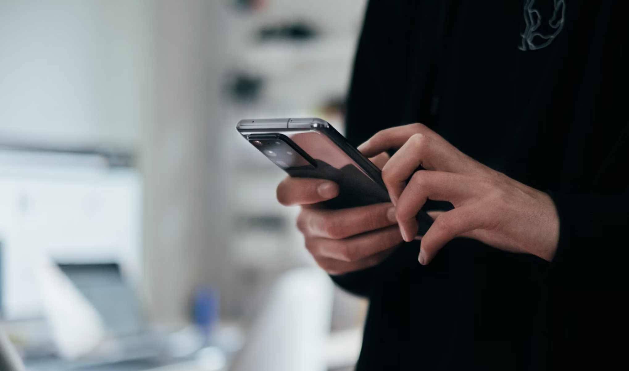 Persona usando smartphone, vista parcial, fondo borroso.