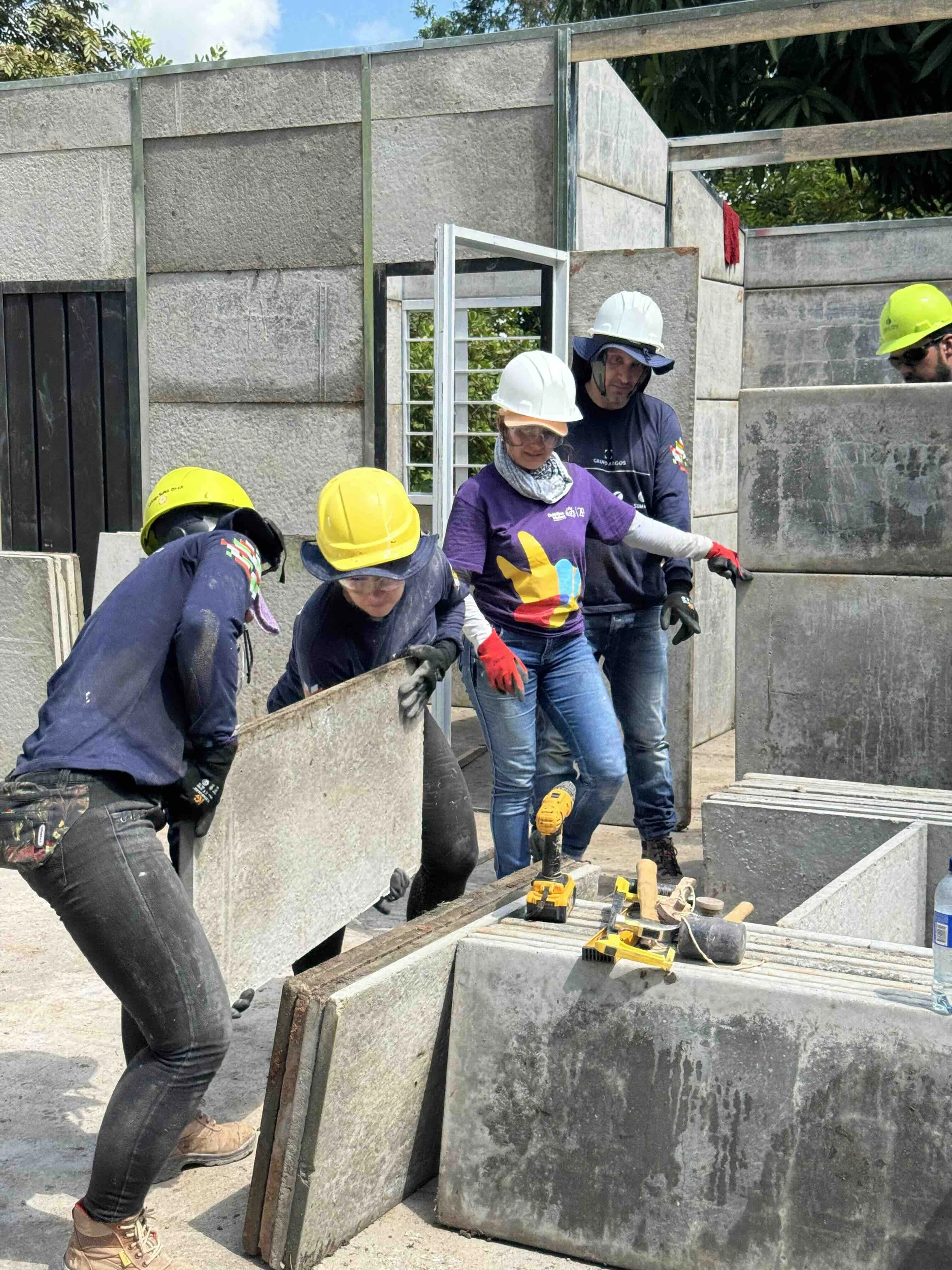 Trabajadores en construcción ensamblando muros de concreto con herramientas eléctricas y equipo de protección personal.